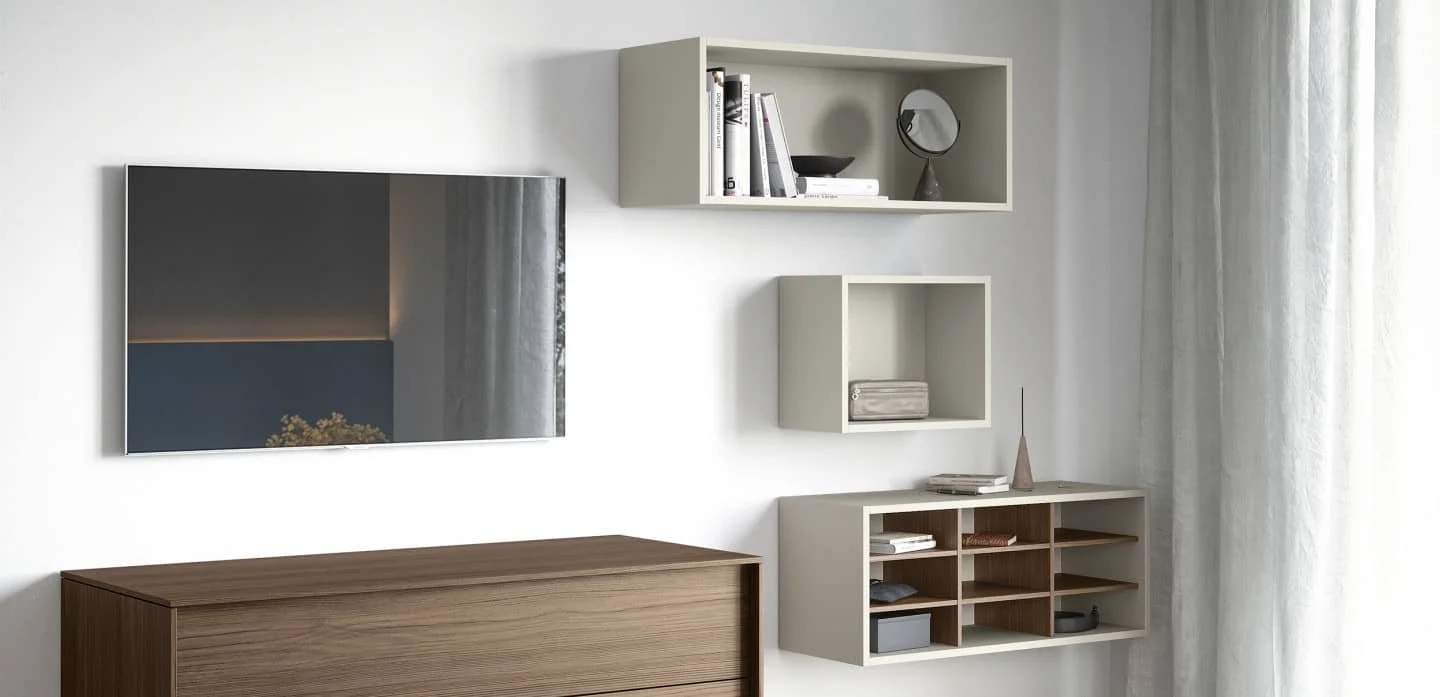 Modern living room wall with a flat-screen TV, white wall-mounted shelves holding books and decor, and a wooden cabinet underneath, with light-coloured curtains on the side.
