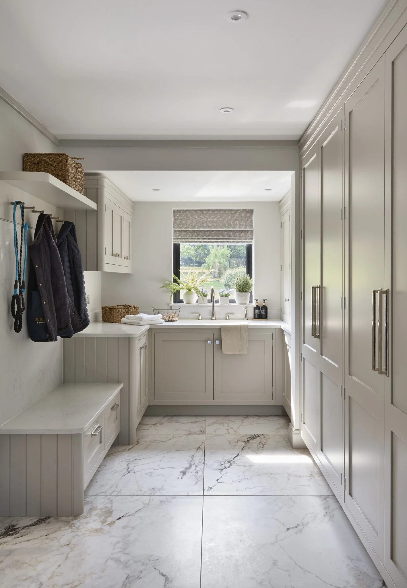 Bright laundry or utility room with white cabinetry, marble tile flooring, and a window with potted plants on the windowsill.