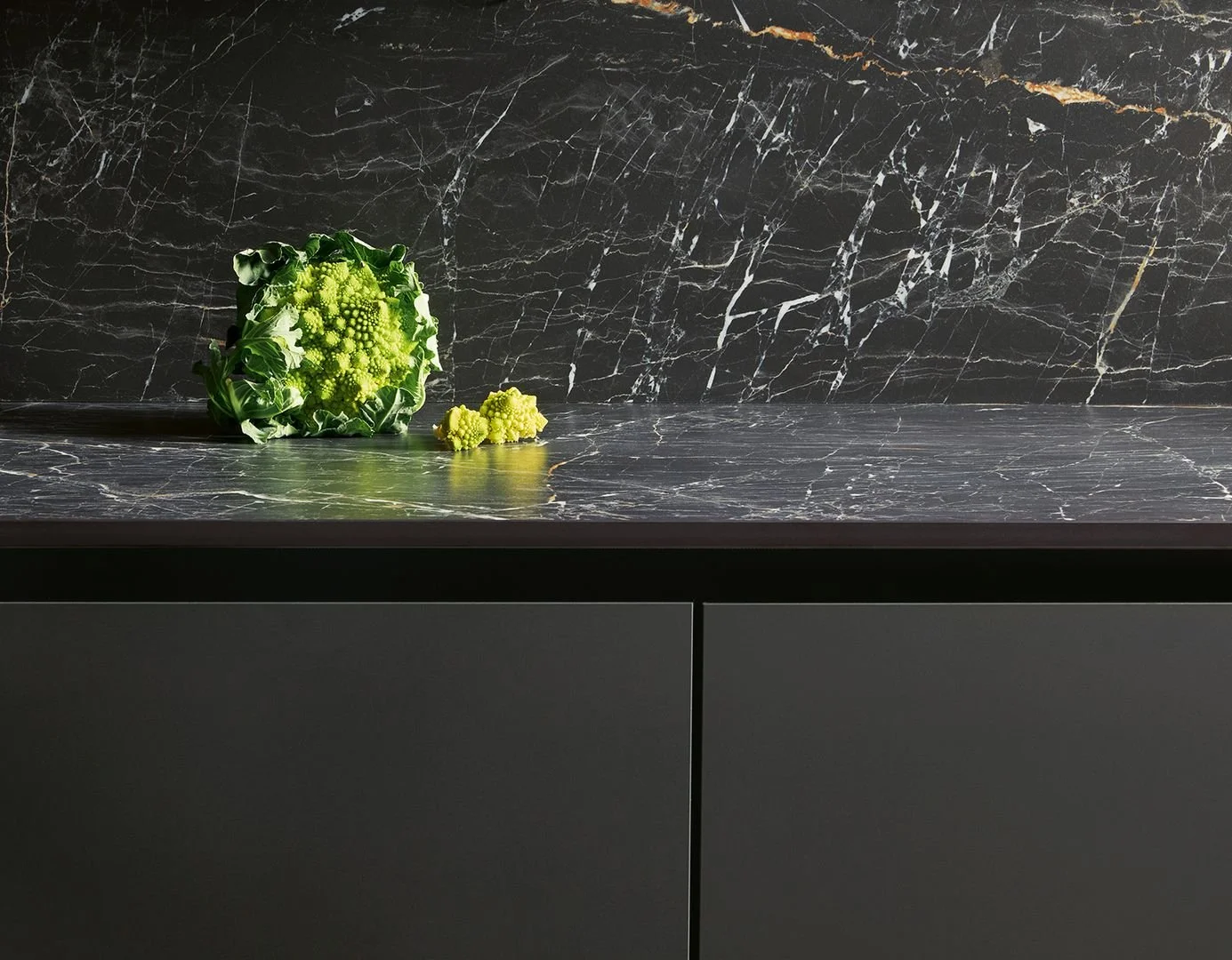A decorative green Romanesco cauliflower on a black marble countertop with a matching black marble backsplash.