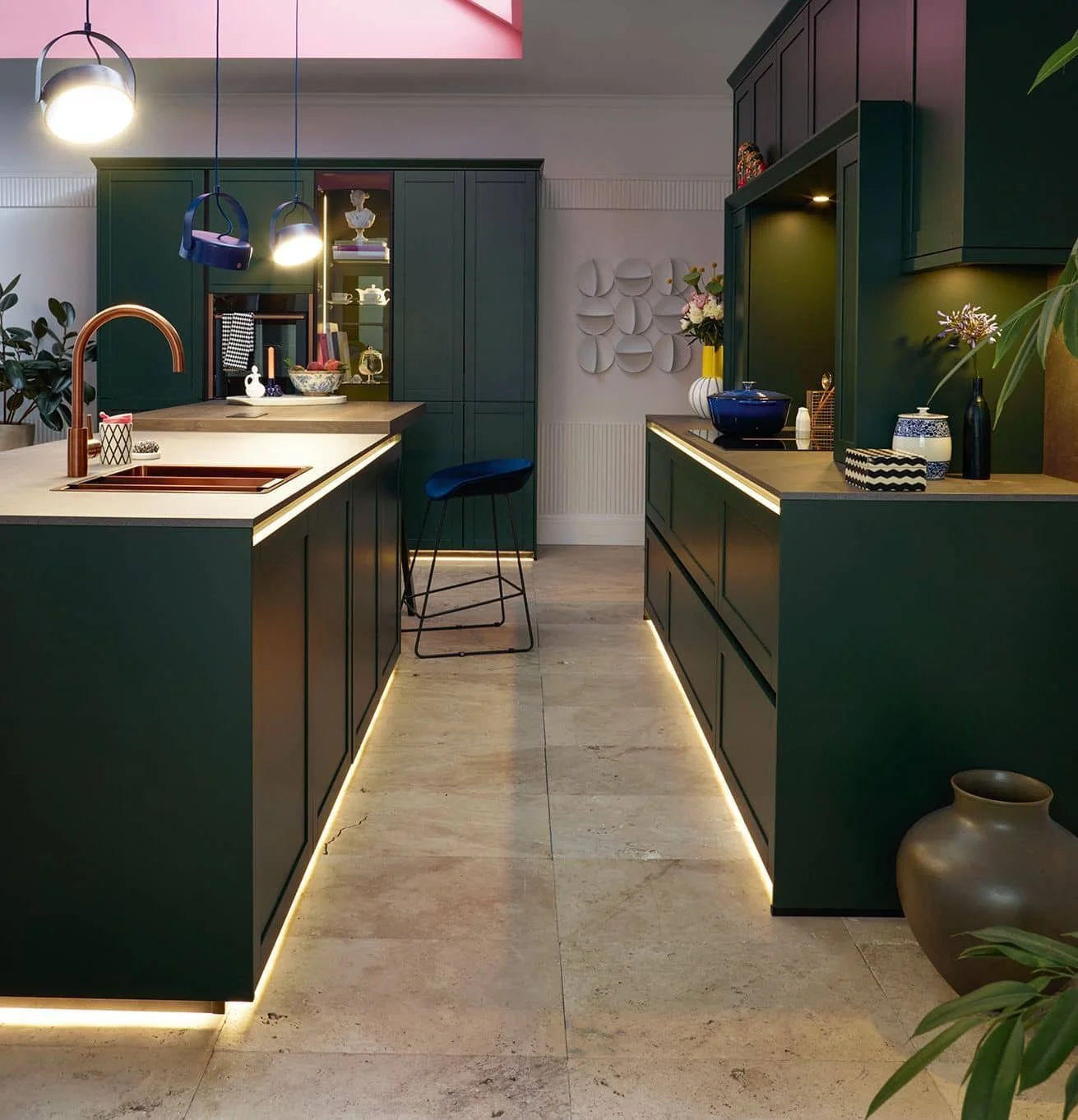 Modern kitchen with dark green cabinets, beige countertops, under-cabinet lighting, and decorative items including vases and bowls.