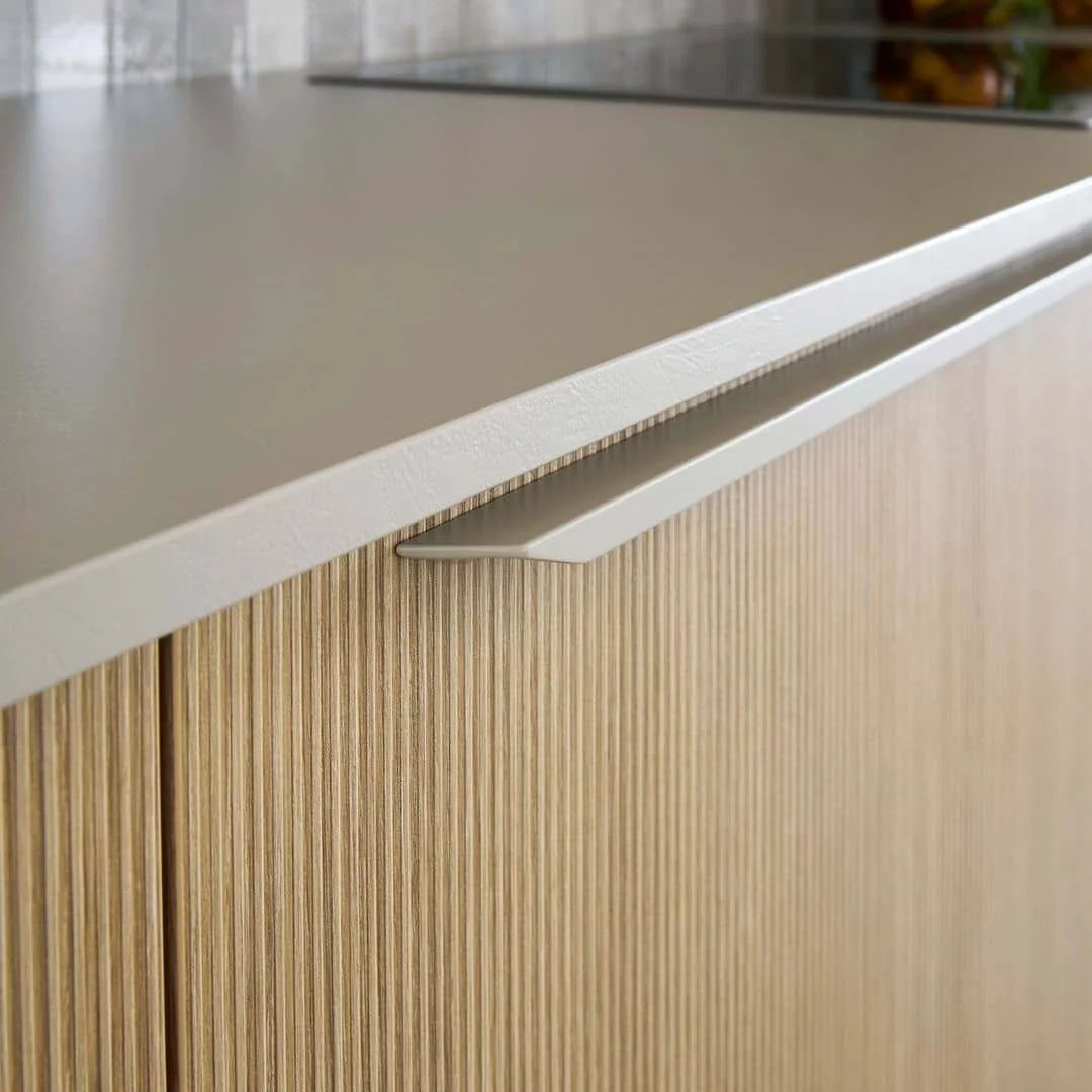 Close-up of a wooden cabinet with a textured light wood finish and a white countertop with a modern floating handle.