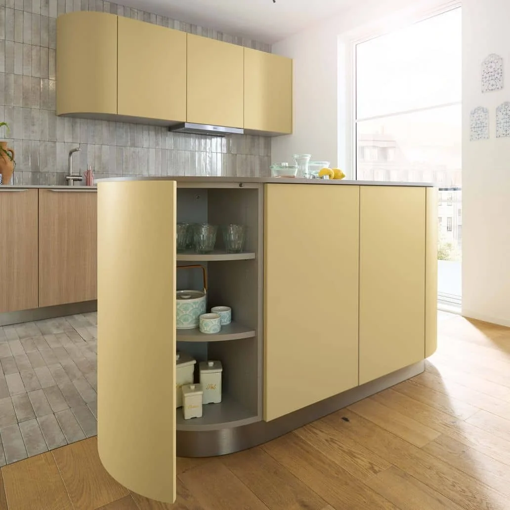Modern kitchen with yellow and wood cabinetry near a large window, featuring open shelves with glassware and decorative containers, and a tiled backsplash.