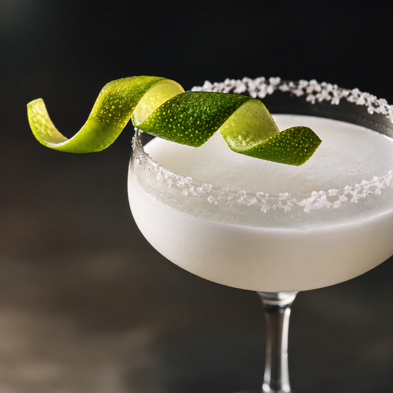 Copa de margarita decorada con borde de sal y una espiral de cáscara de lima