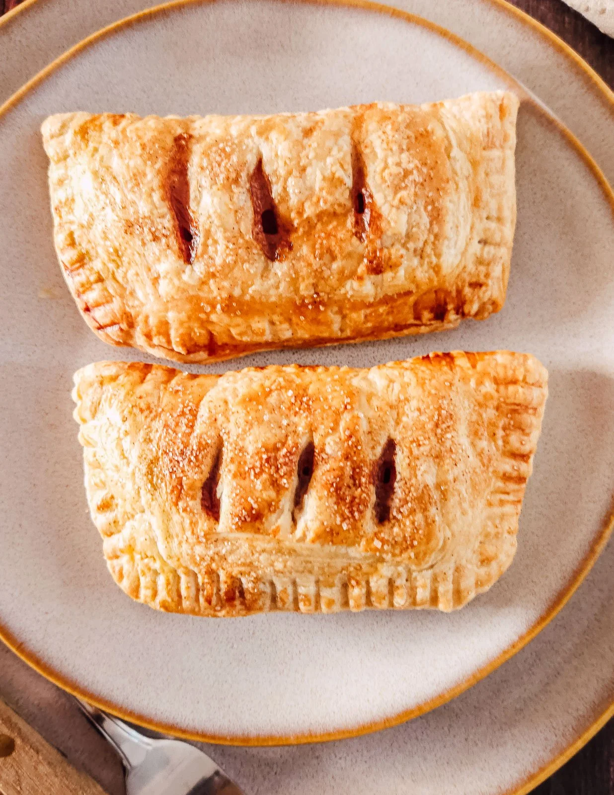Close-up of two rectangular apple puff pastry hand pies showing flaky layers and glossy apple filling.