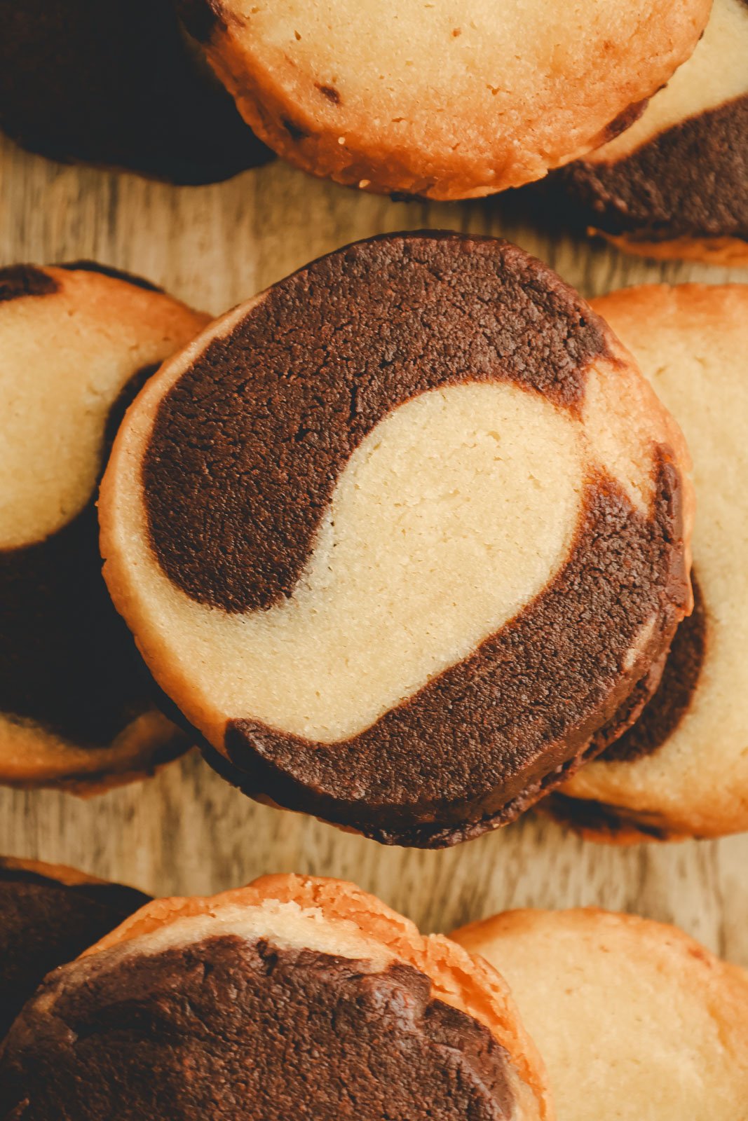 Top-down flat lay of three marble sablé sandwich cookies with vanilla and chocolate swirls, arranged in a pyramid formation on a wooden board.