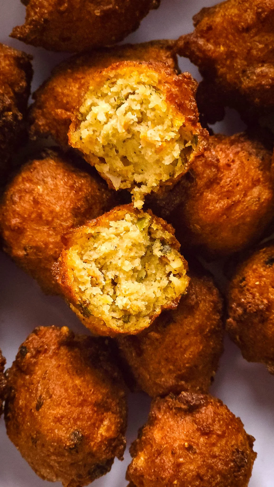 Diagonal arrangement of dudhi pakoda on a white plate, fresh dudhi leaves laid diagonally across the plate, green chutney bowls bottom-left and top-right, with two spoons placed alongside