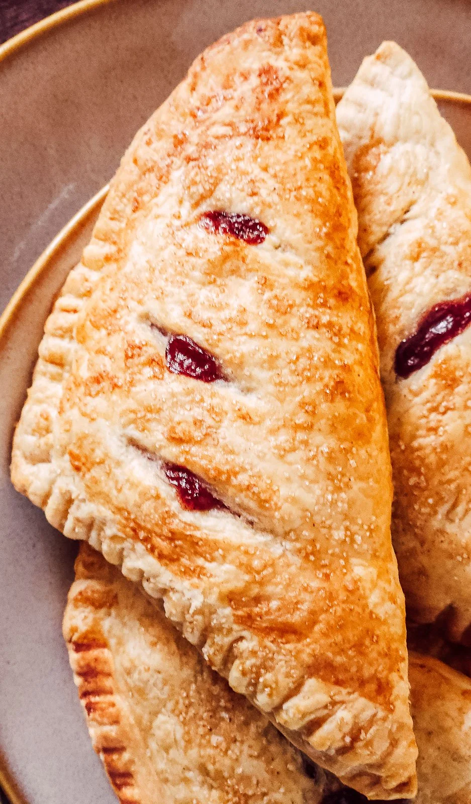 Close-up of triangular apple and blueberry turnovers with crisp puff pastry layers, golden edges, and jammy fruit filling oozing through the slits.