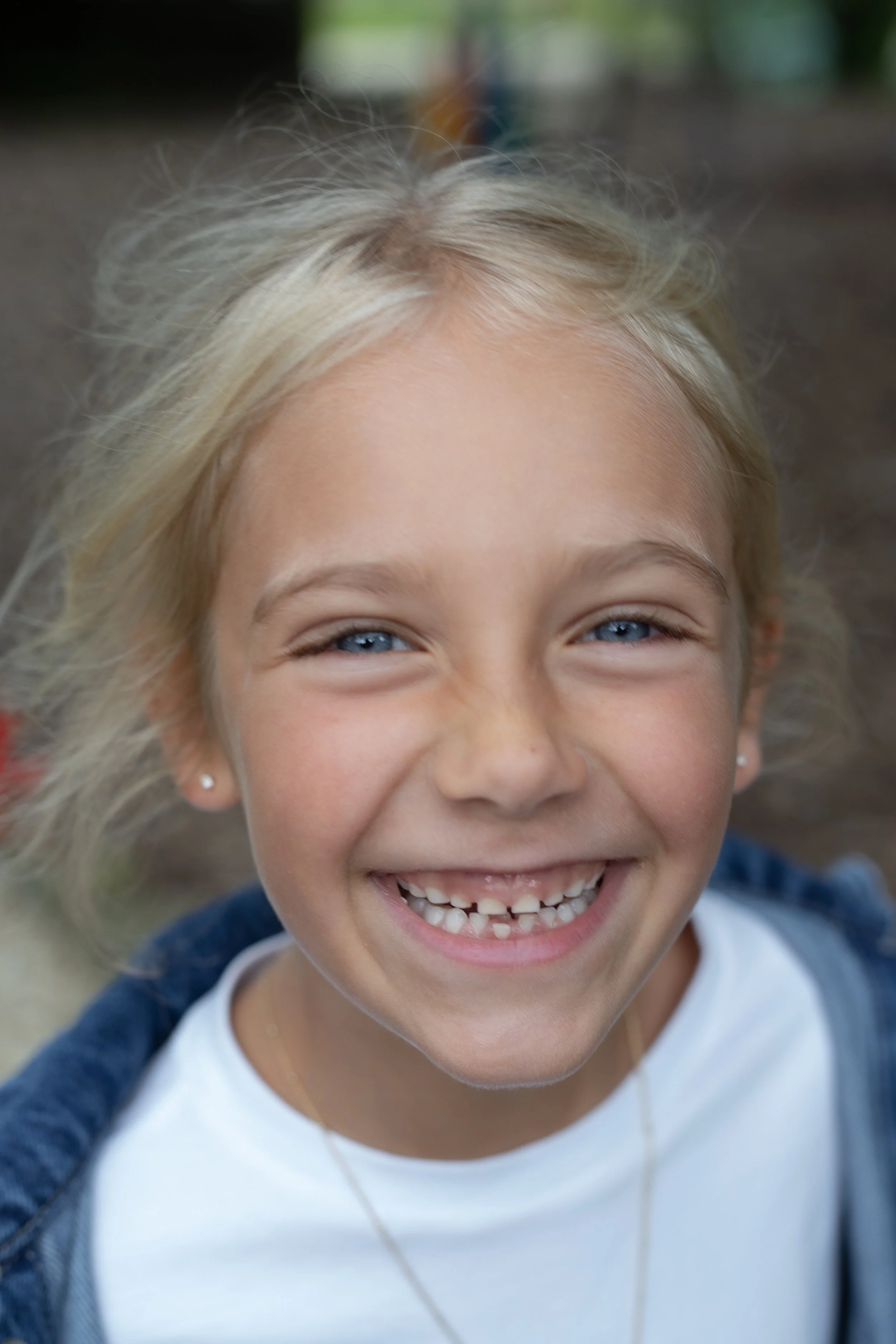 Close-up of a young girl with blonde hair and blue eyes smiling broadly, showing missing teeth.