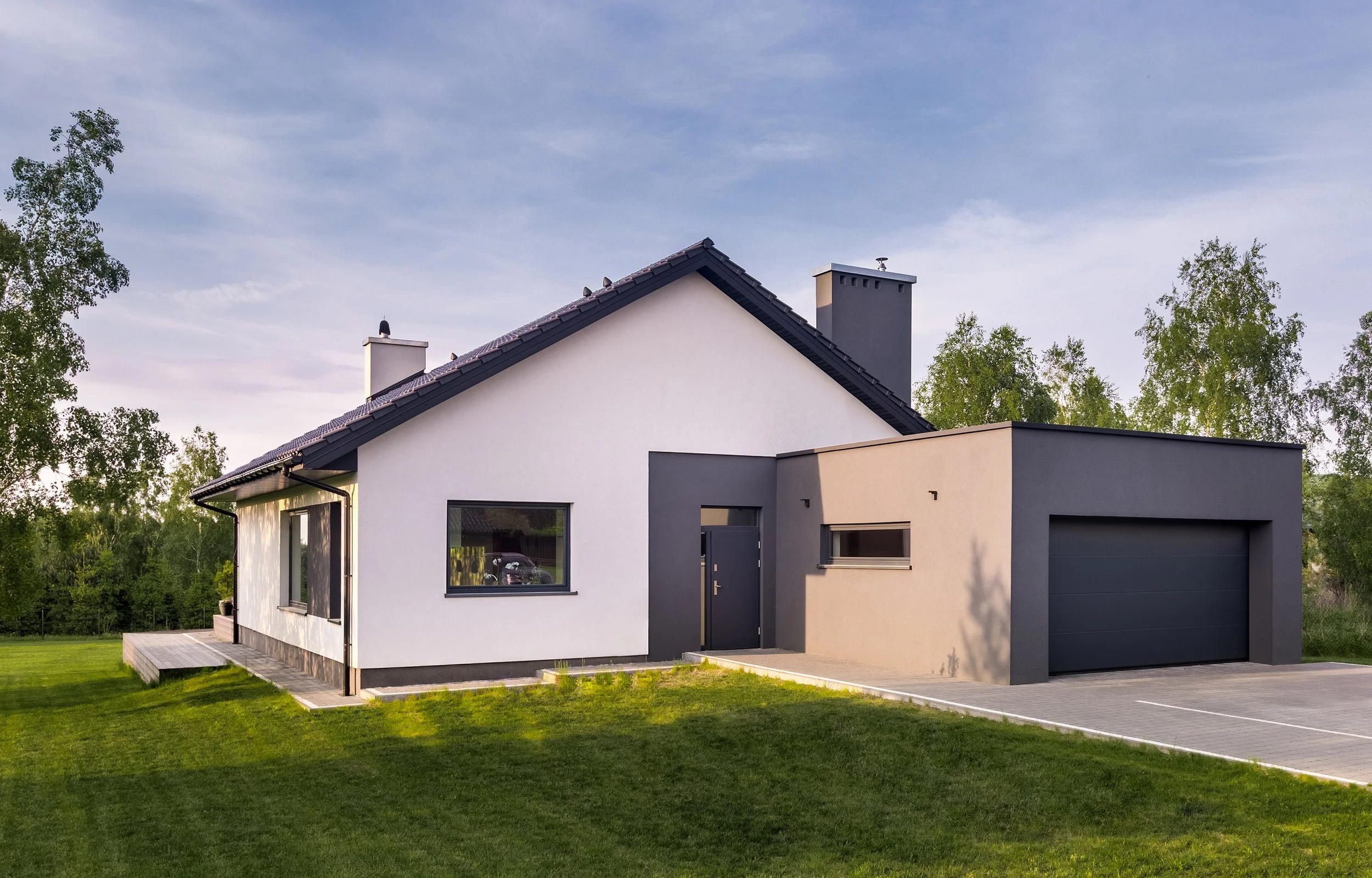 Modern house with white and dark gray exterior, black window frames, a garage, and a well-maintained lawn with green trees in the background.