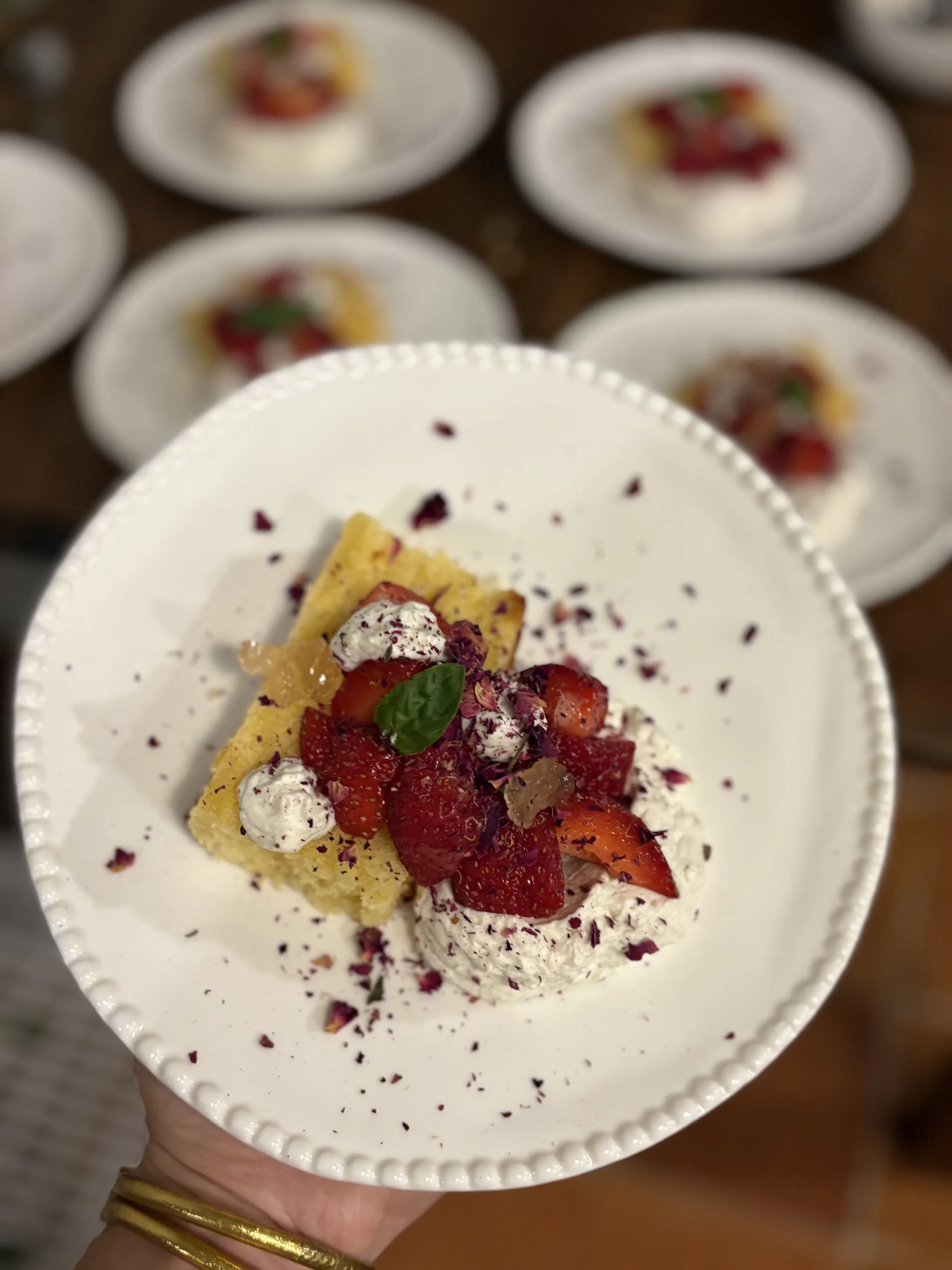 Partie d'un gâteau décoré avec des fraises, de la crème et des pétales de rose séchés, sur une assiette blanche