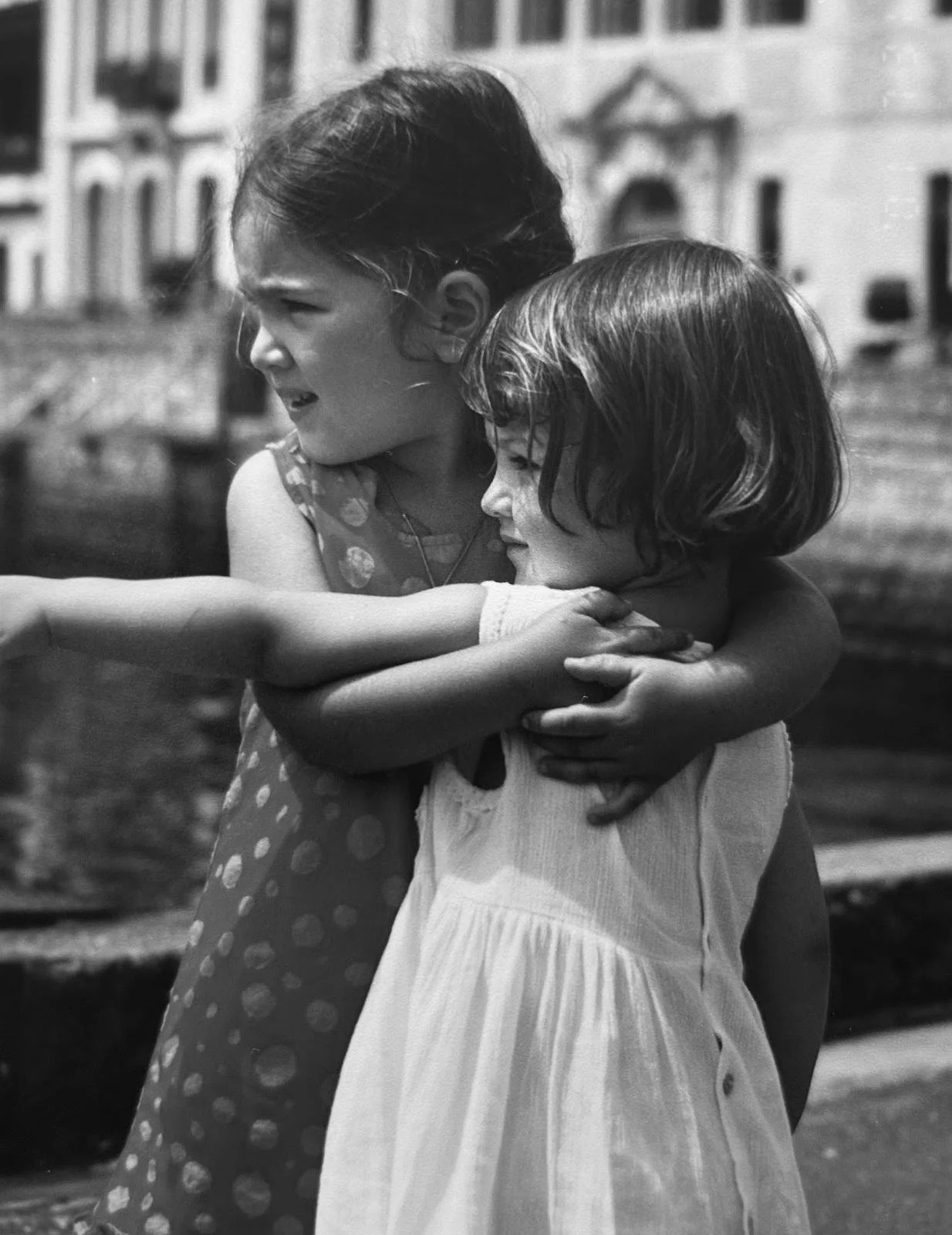 Deux jeunes filles s'enlacent et se réconfortent dans un cadre urbain, en noir et blanc.