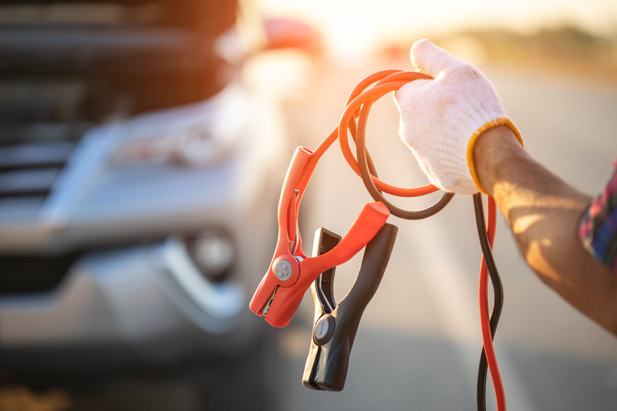 Person holding jumper cables, preparing to jump-start a car during sunset.