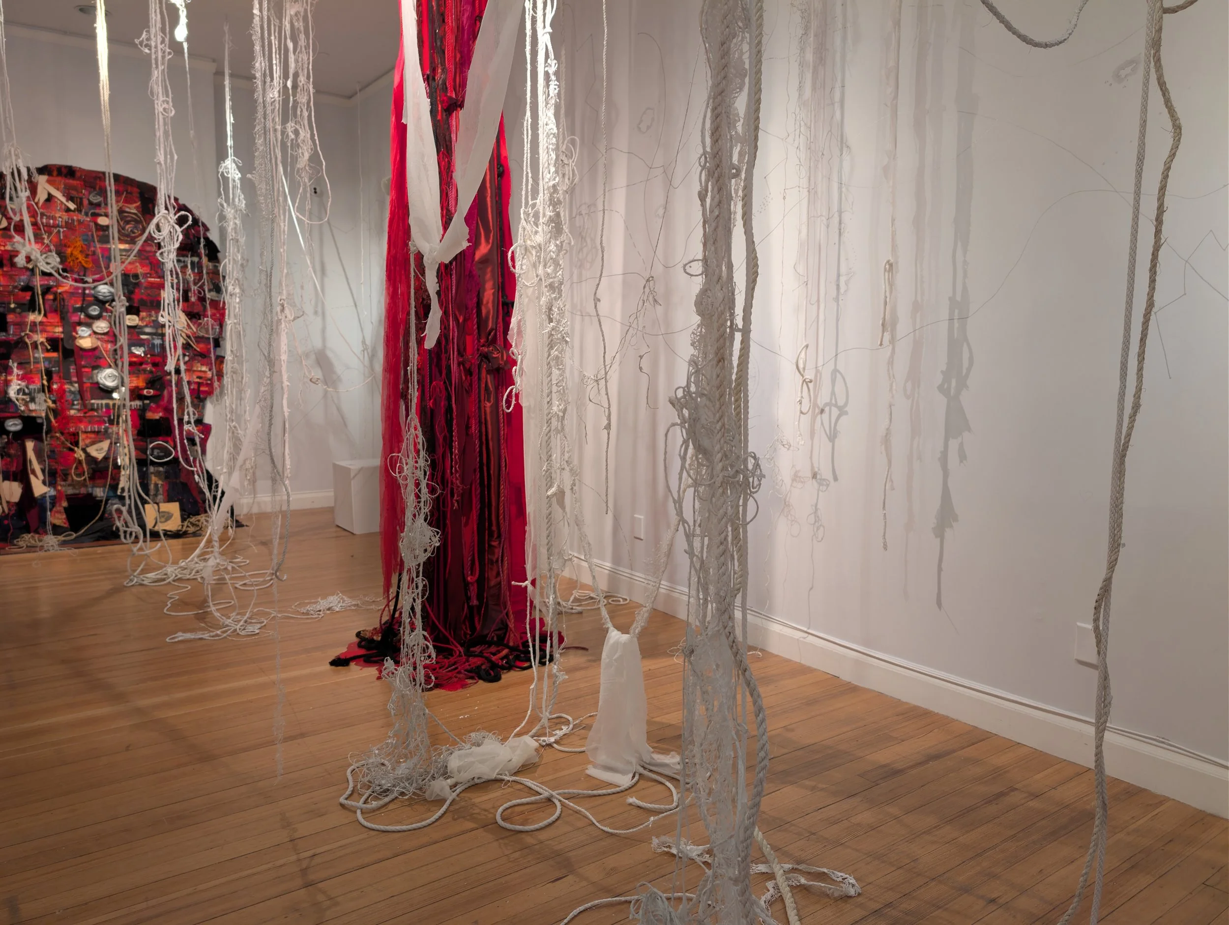 an art exhibit with hanging pieces of fabric, mostly white, a one red curtain