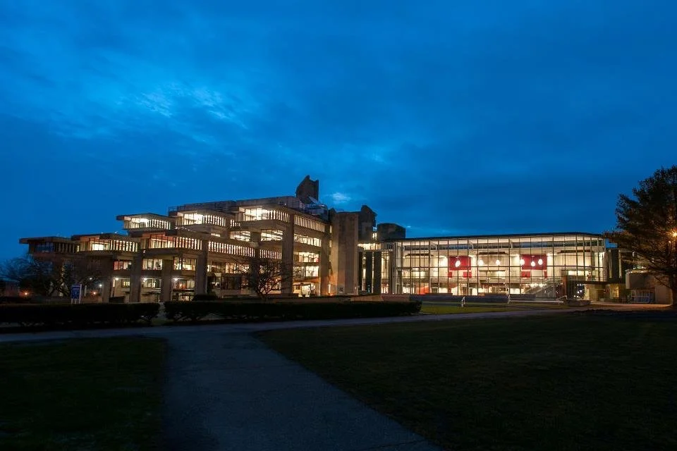 A modern  building of Claire T. Carney Library in UMass Dartmouth illuminated at dusk under a deep blue evening sky.
