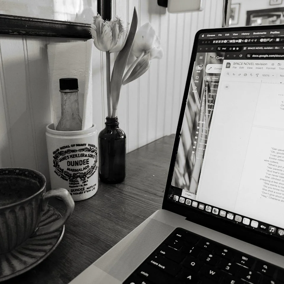 Black-and-white photo of a laptop displaying a document beside a coffee cup and flowers.