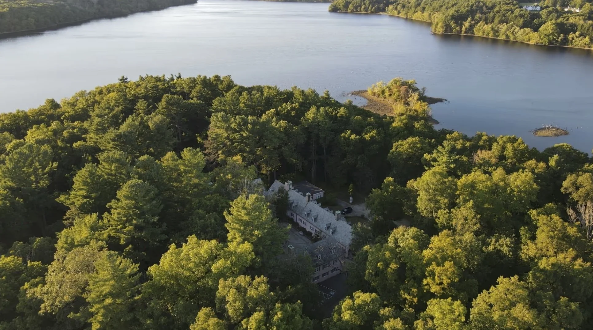 A forested peninsula surrounded by a lake, with buildings nestled among the trees and small islands visible in the water.