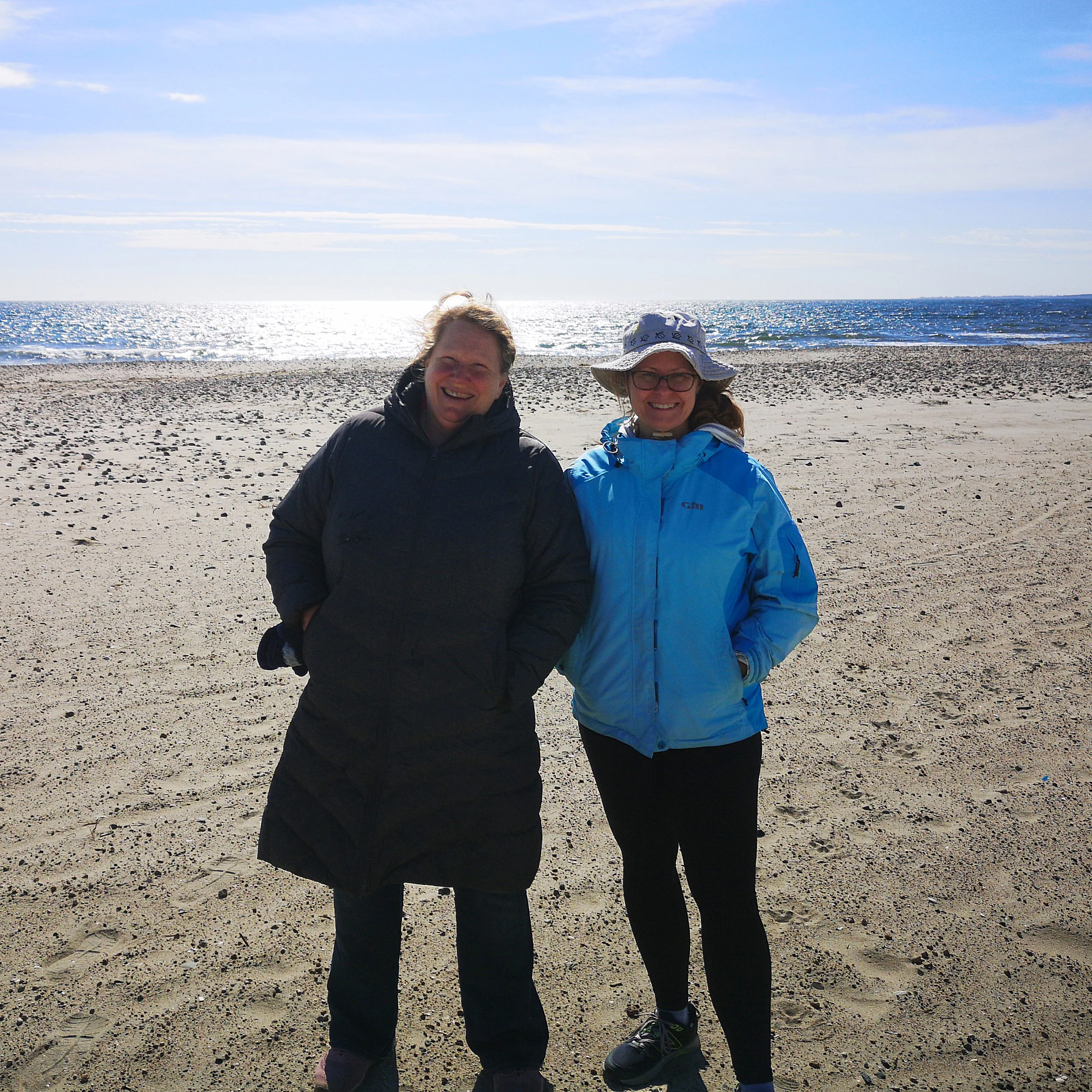 Midori Evans and Krista Allen standing on a beach with the ocean and shoreline in the background