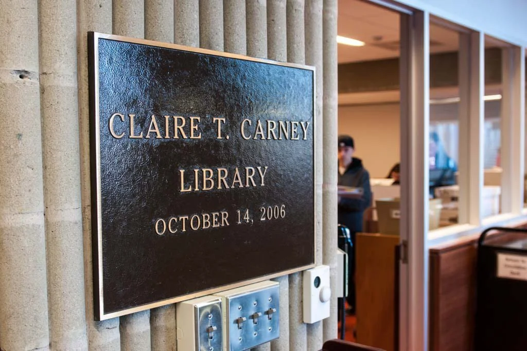 Plaque reading “Claire T. Carney Library” mounted beside a library entrance.