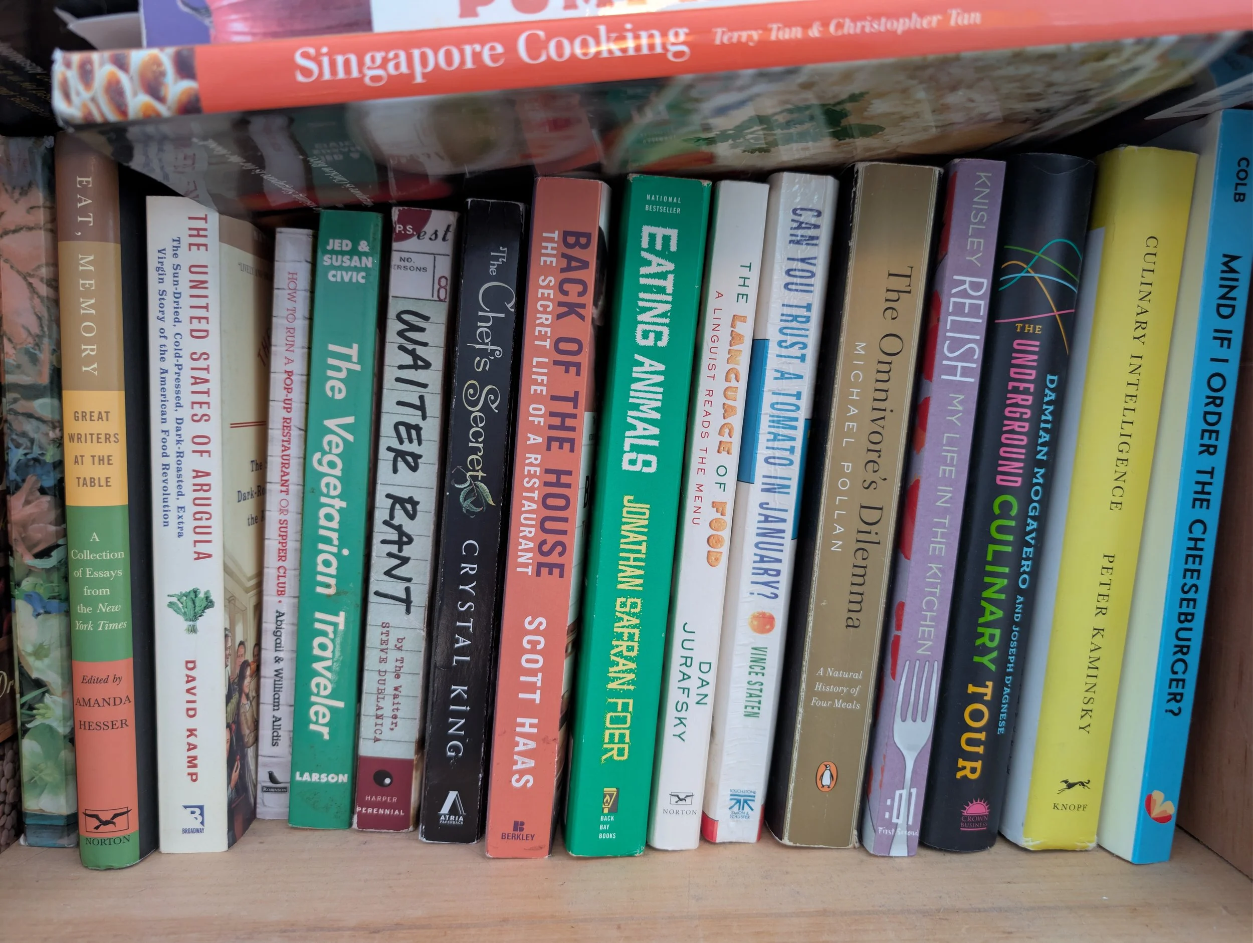 Close-up of a bookshelf with tightly packed books, including several titles about cooking and food.