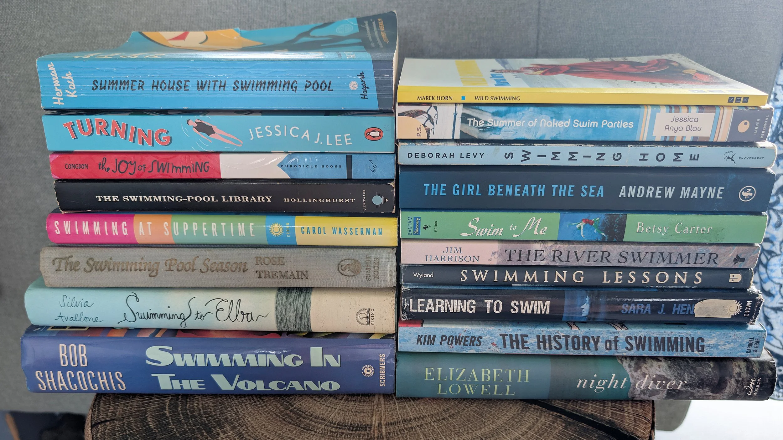 A stack of books about swimming, pools, and water-themed stories arranged on a wooden surface.