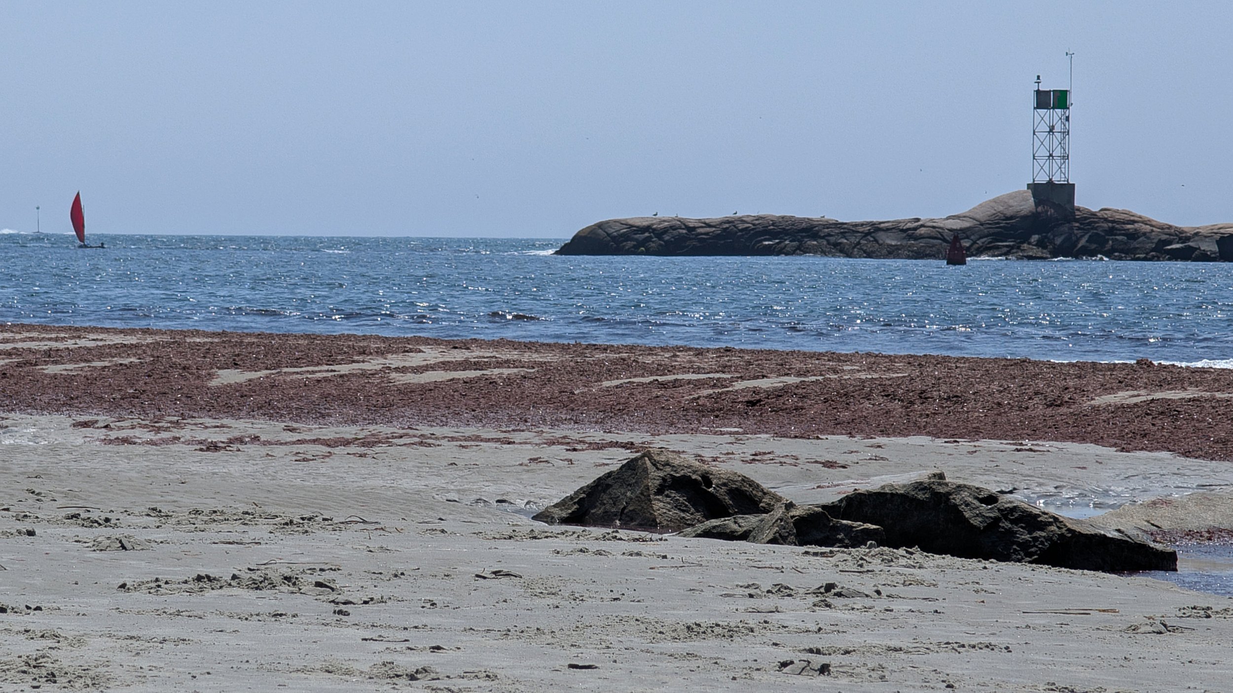 A sandy beach with rocky shoreline, calm blue water, and a small rocky island