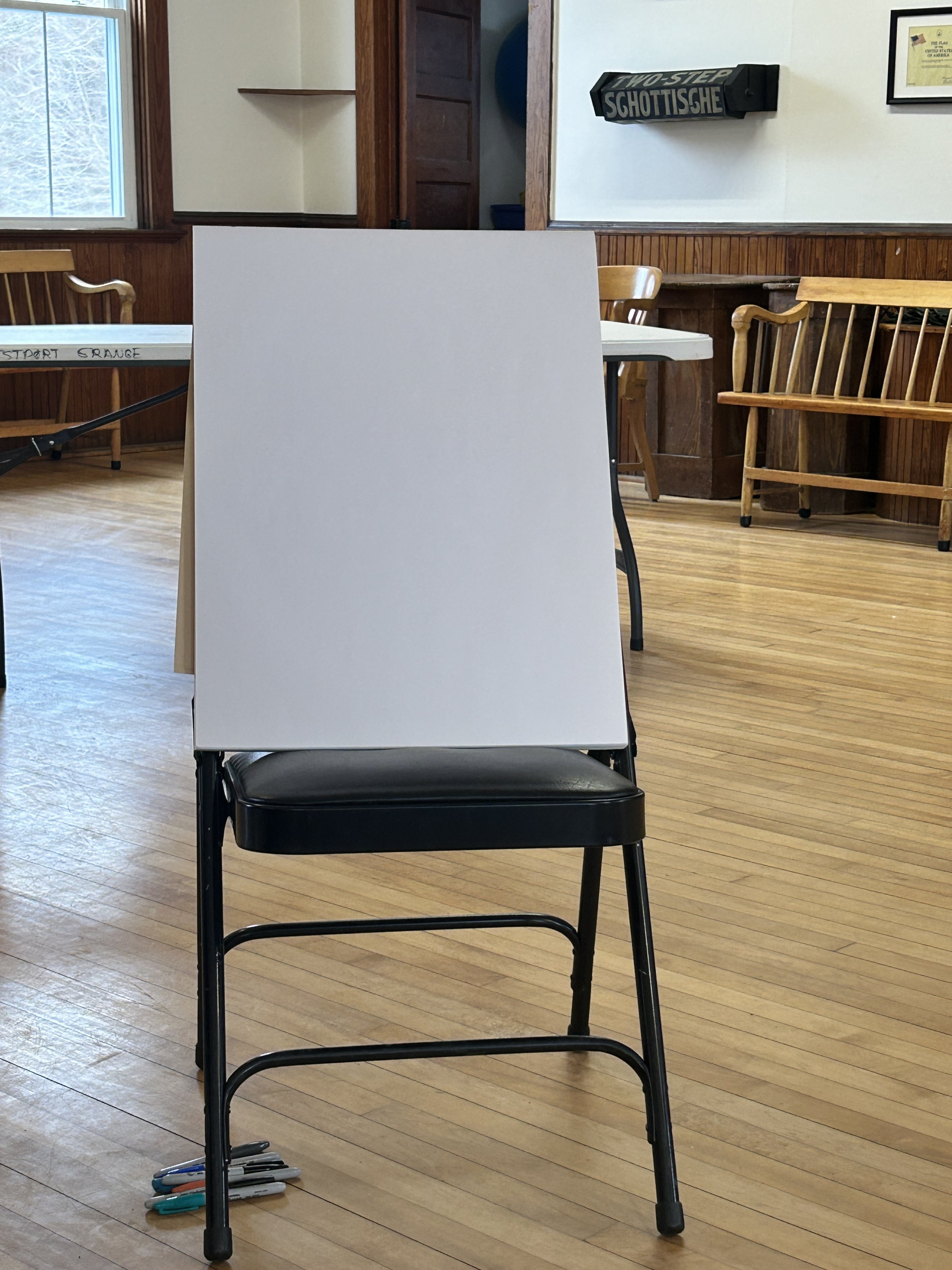 A large, blank white board or canvas sits propped up on a black folding chair.