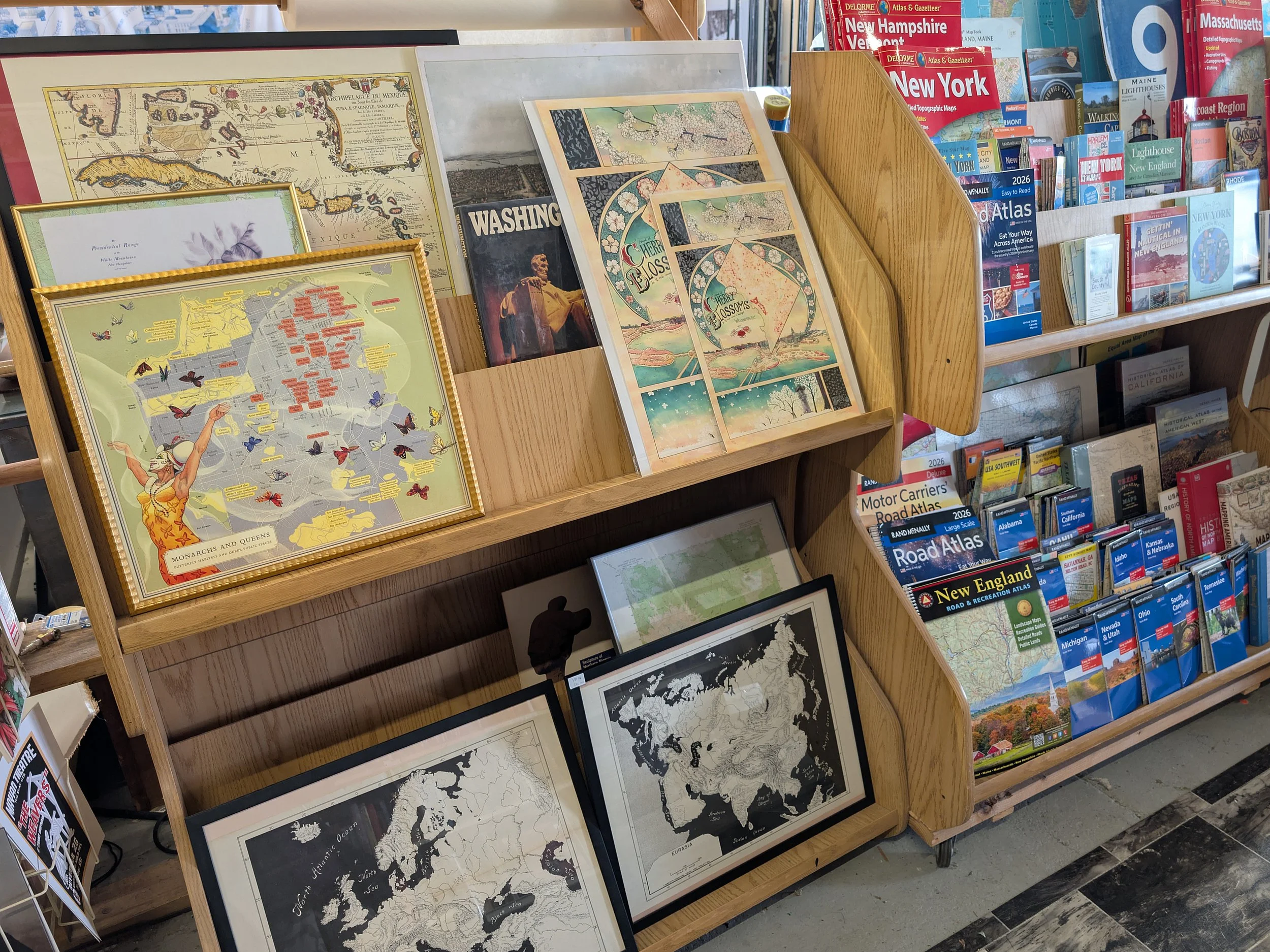 A wooden display shelf filled with framed maps and map-themed prints.