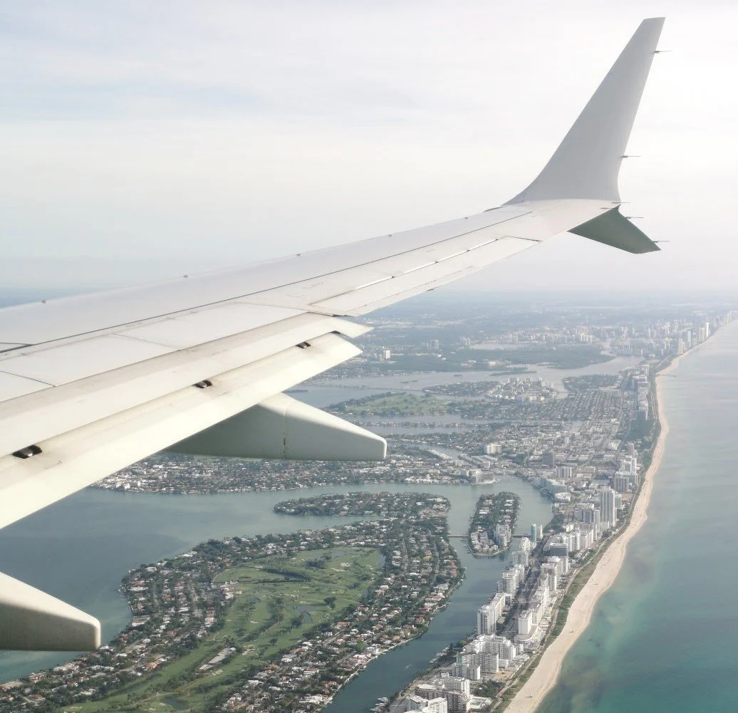 View from an airplane window showing the wing above a coastal city.