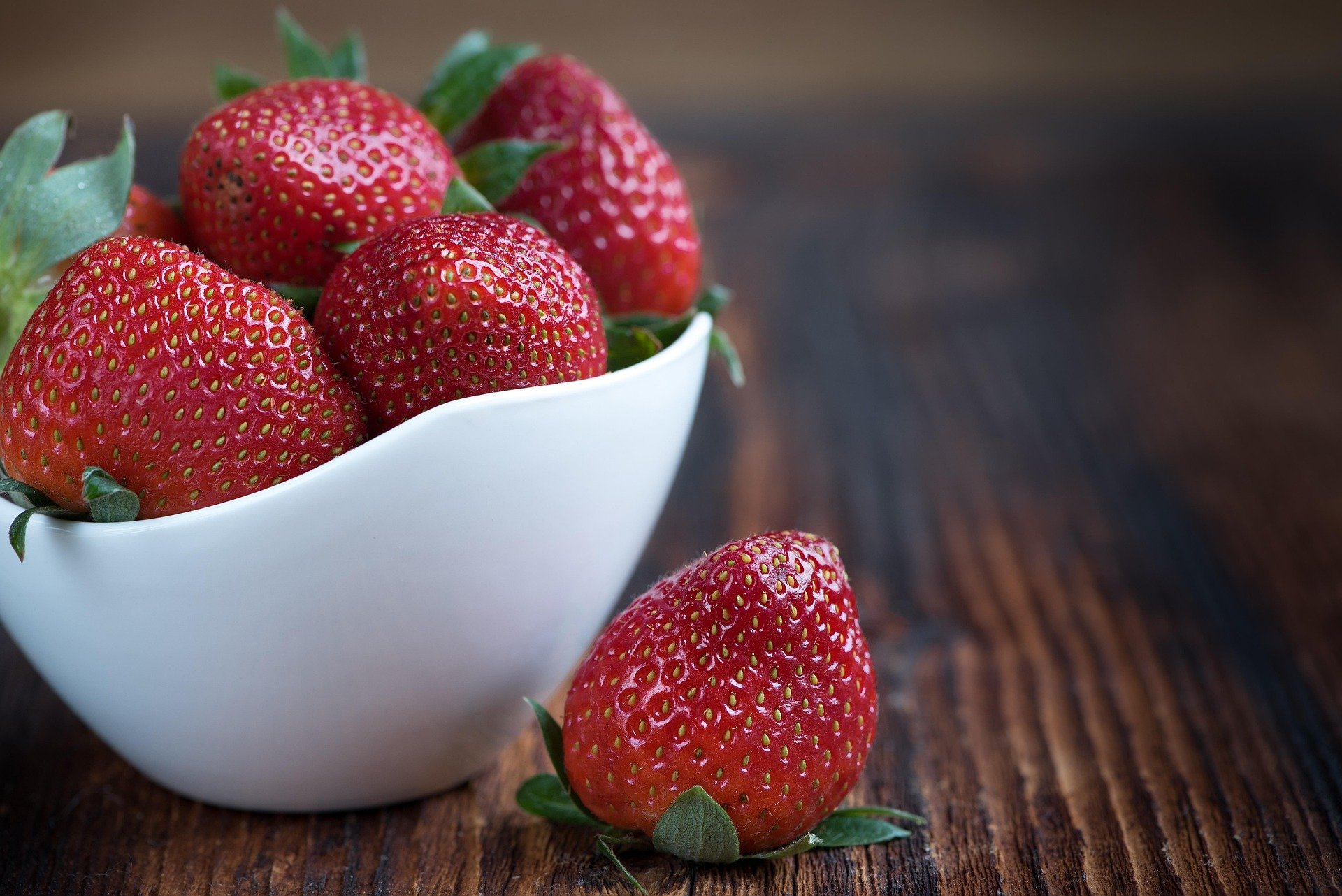 Close-up of fresh strawberries in a white bowl on a wooden table.
