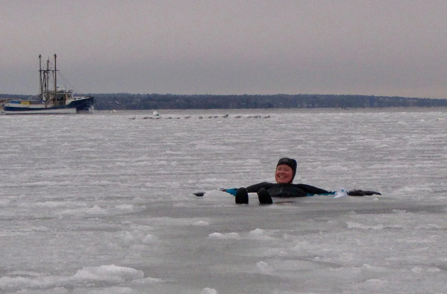 Melinda Green in a wetsuit and swim cap smiling while floating in icy, partially frozen water.