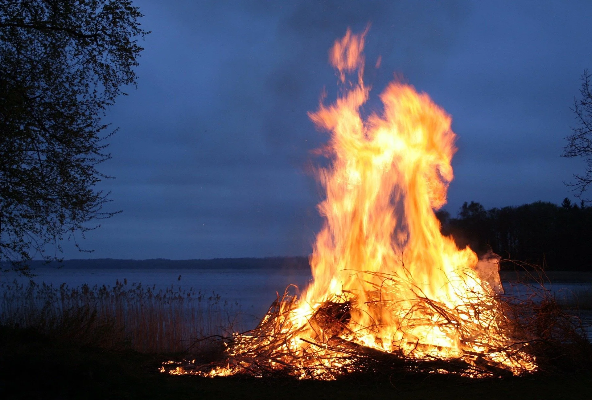 Bright bonfire burning outdoors near a lake at dusk.