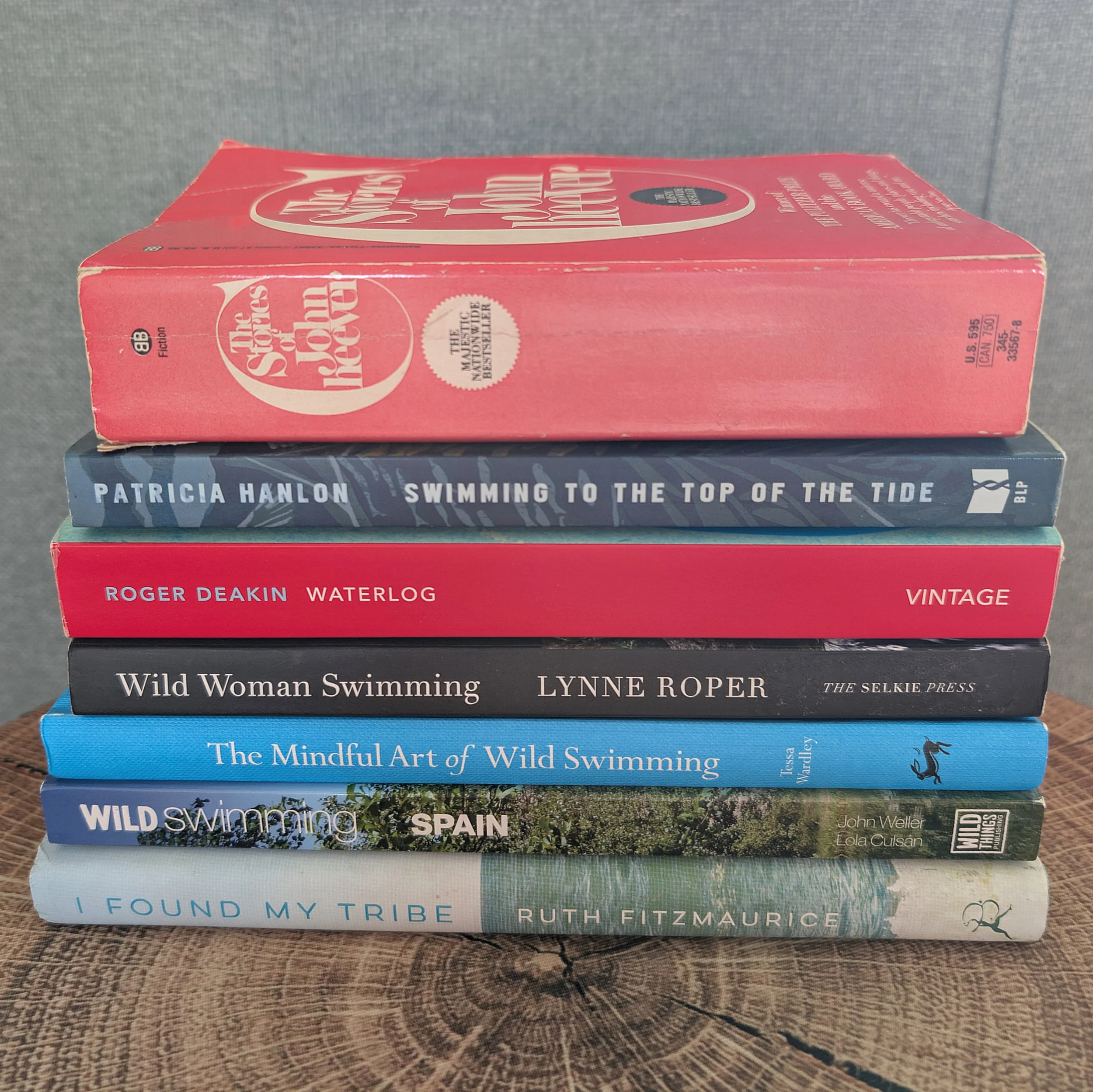 A stack of books about wild swimming and water, including Swimming to the Top of the Tide, Waterlog, Wild Woman Swimming, The Mindful Art of Wild Swimming, and I Found My Tribe.