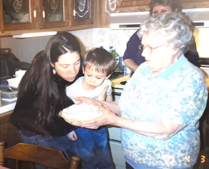 The author Sarah Kiepper and a child sit together in a kitchen while an older woman holds a pie in front of them.