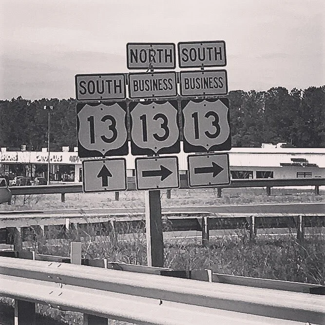 Black-and-white photo of highway route signs for Route 13 showing northbound, southbound, and business route directions.