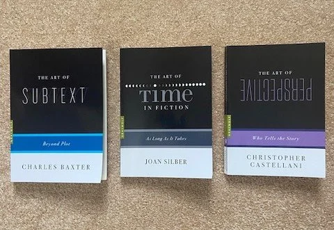 Three books from “The Art of” series about writing, including topics on subtext, time in fiction, and perspective, arranged side by side