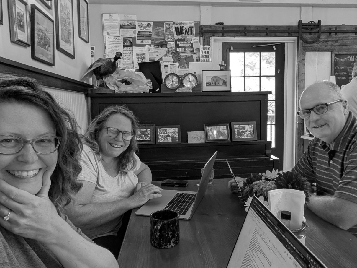 Three people sitting at a table smiling and working on their laptops