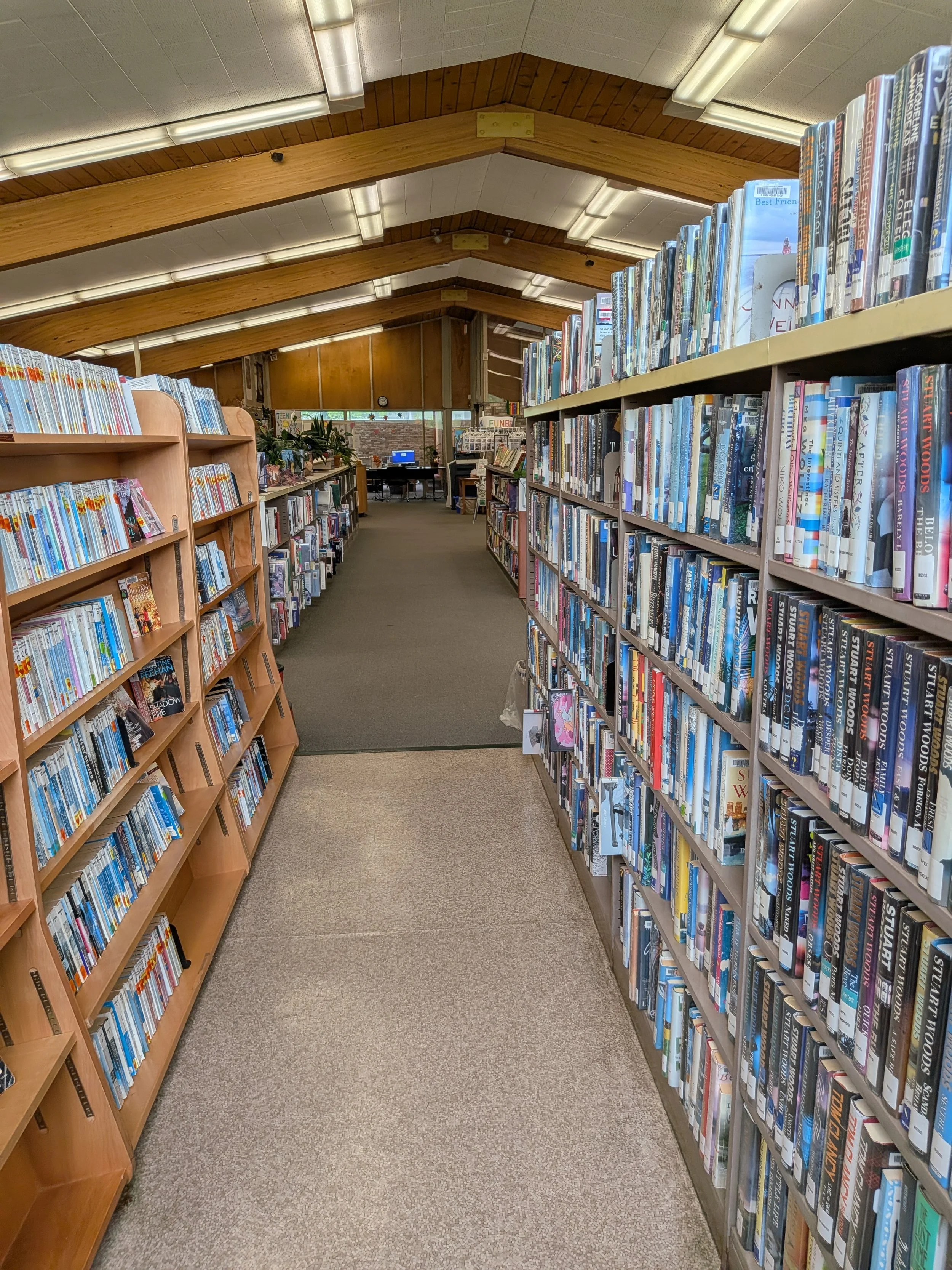 Interior view of a library aisle lined with bookshelves and books under wooden ceiling.