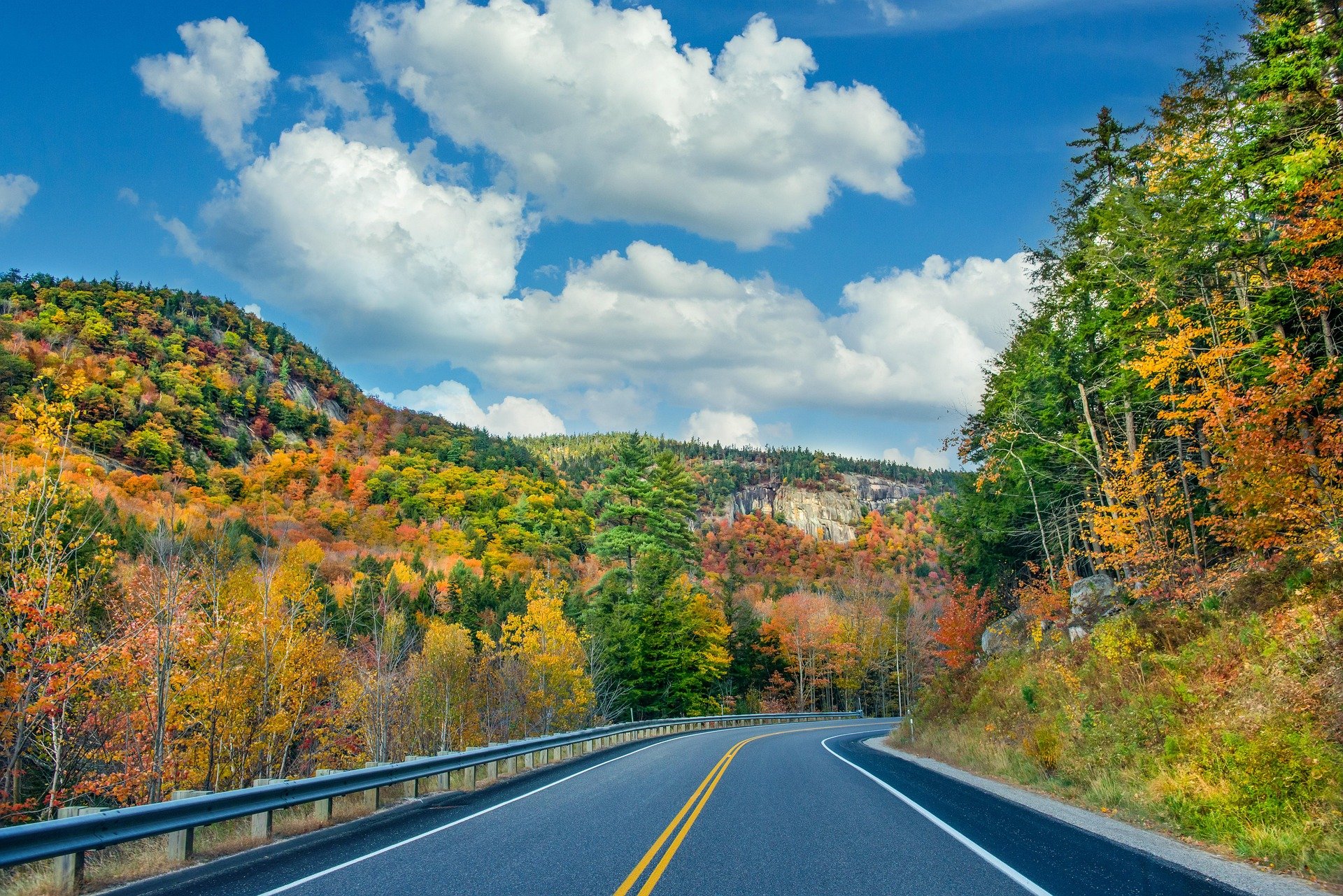 A scenic autumn road winding through colorful forested mountains.