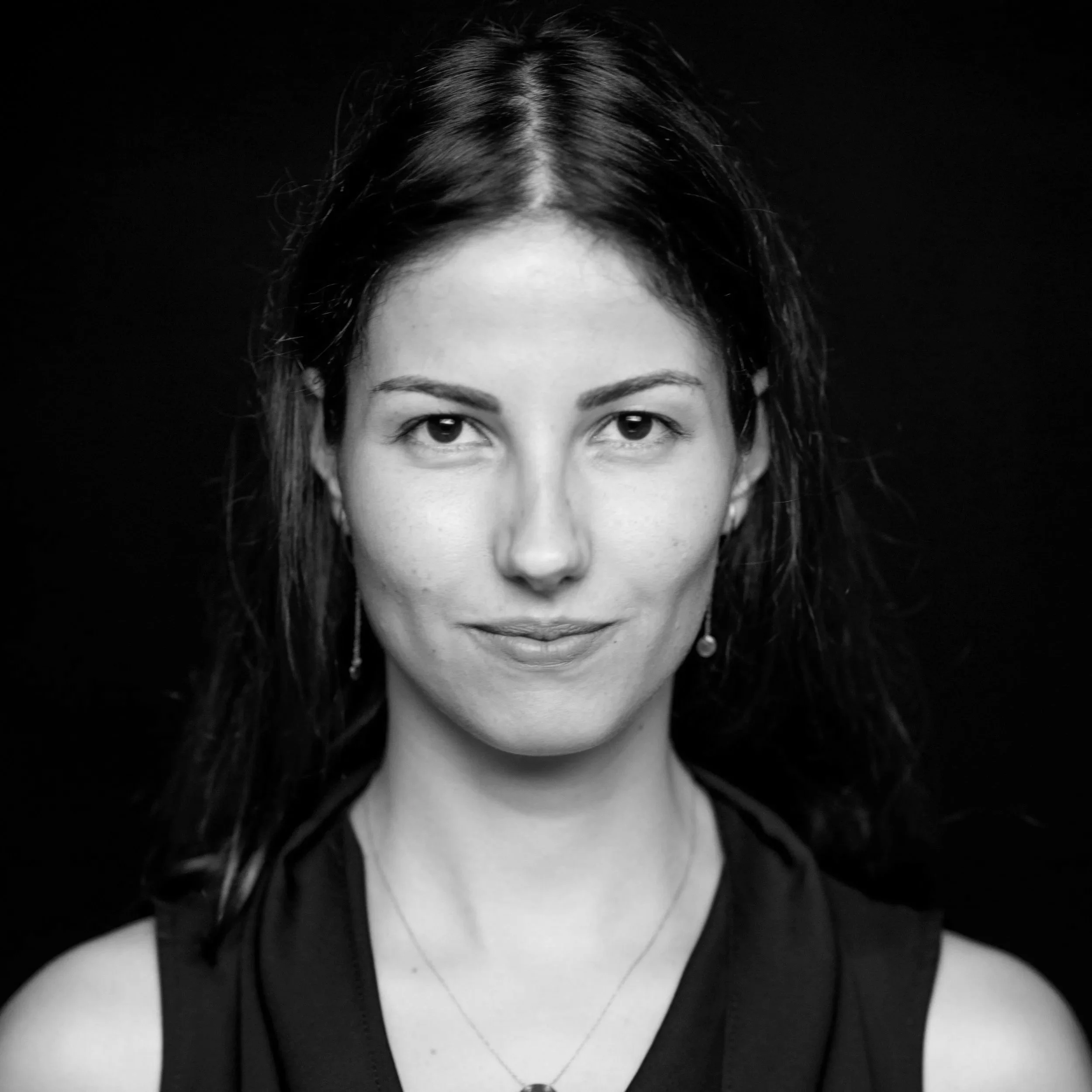 Close-up black-and-white photo of a woman's face and upper shoulders, with a slight smile, wearing a black top and a delicate necklace.