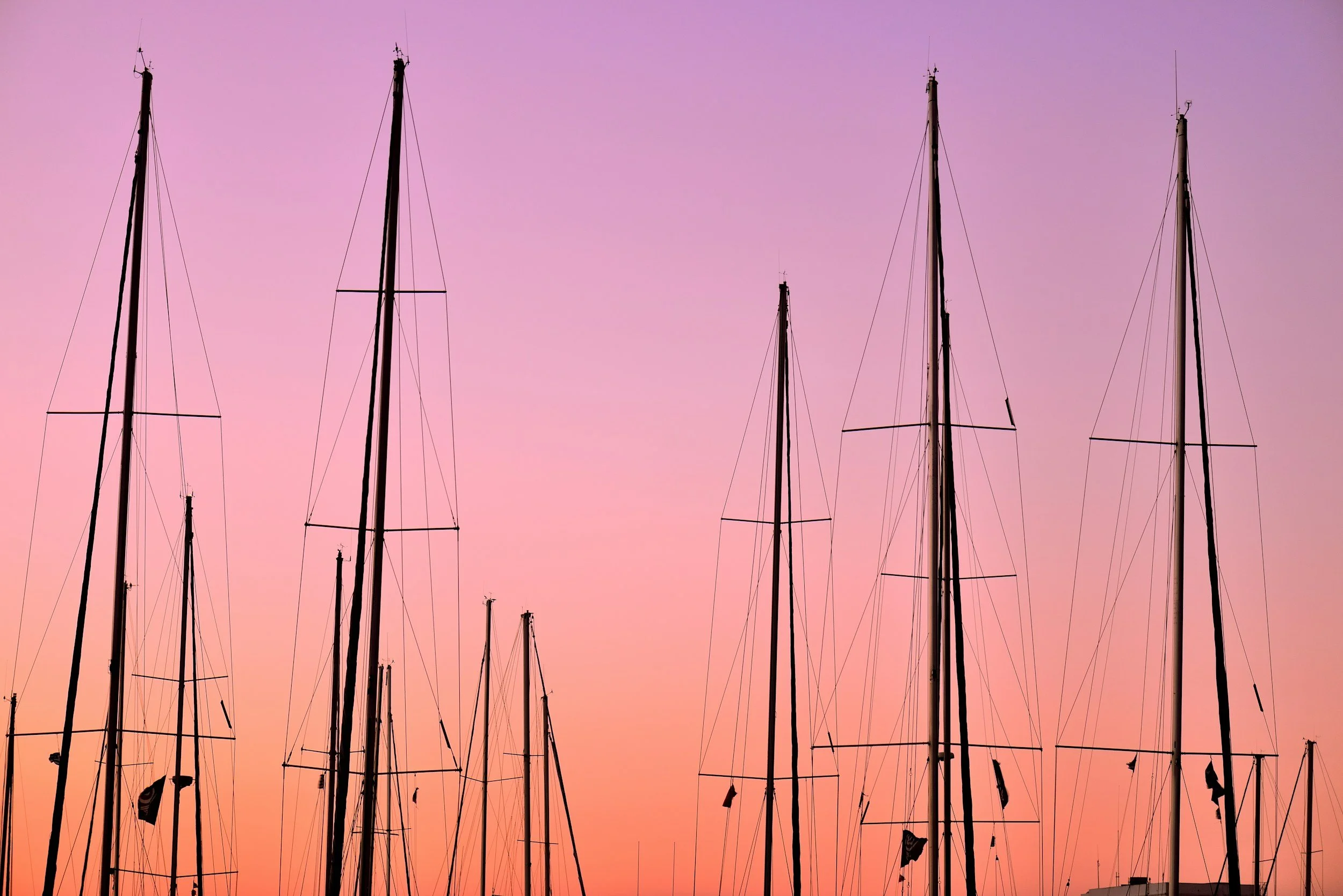 Sailboat masts at sunset with a pink and purple sky in the background.