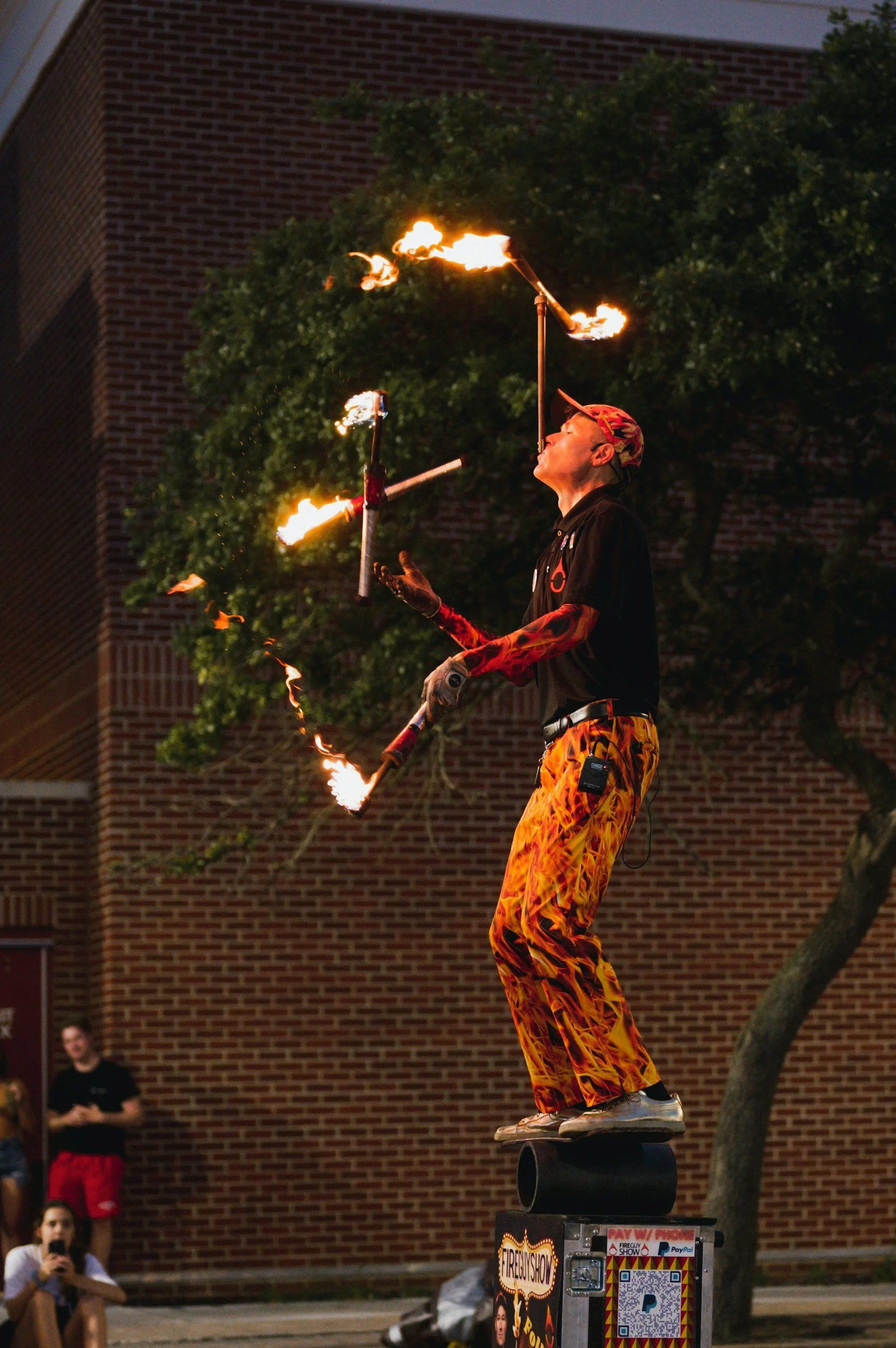 A fire performer balancing on a skateboard on a rolling platform, juggling flaming torches during a fire show event.