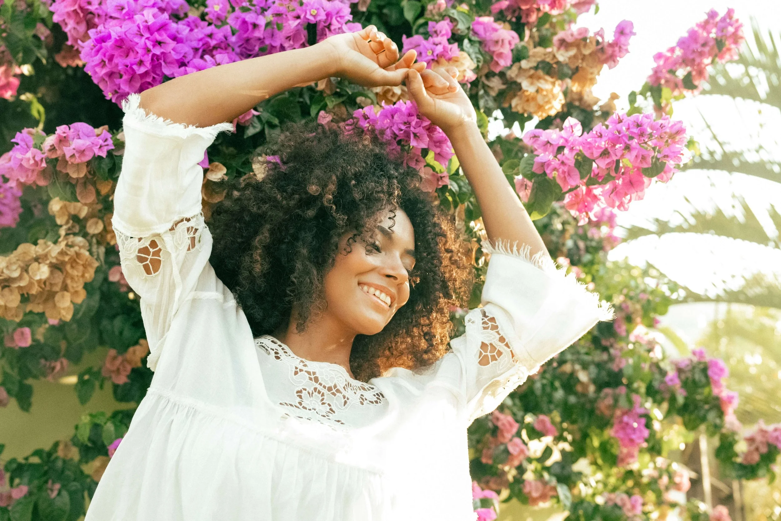 black woman with curly hair outside with purple flowers behind her