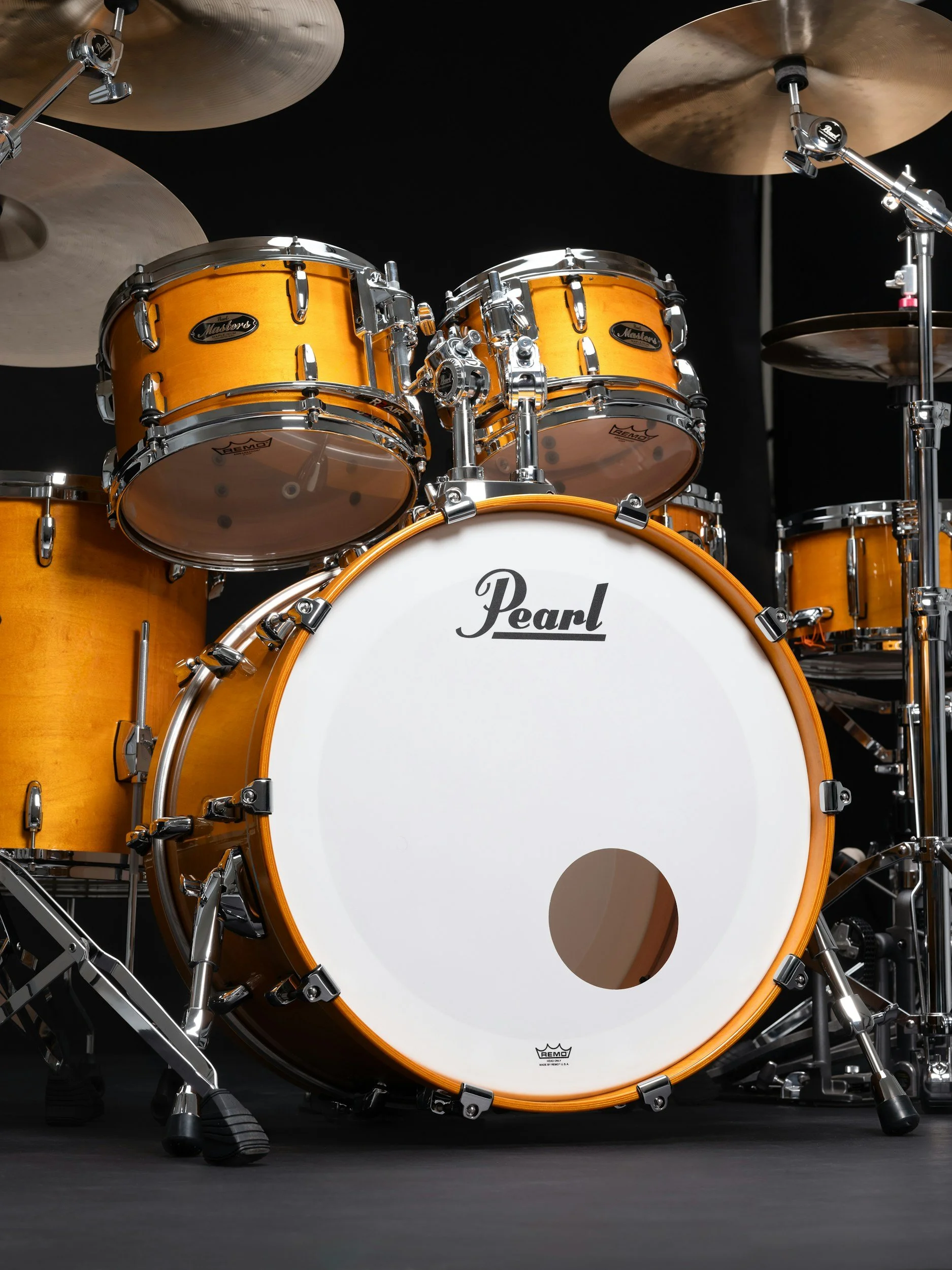 Set di batteria Pearl con bastoni, tamburi in legno di colore arancione e tom-toms, con piatti in ottone sopra e attorno, su sfondo nero.