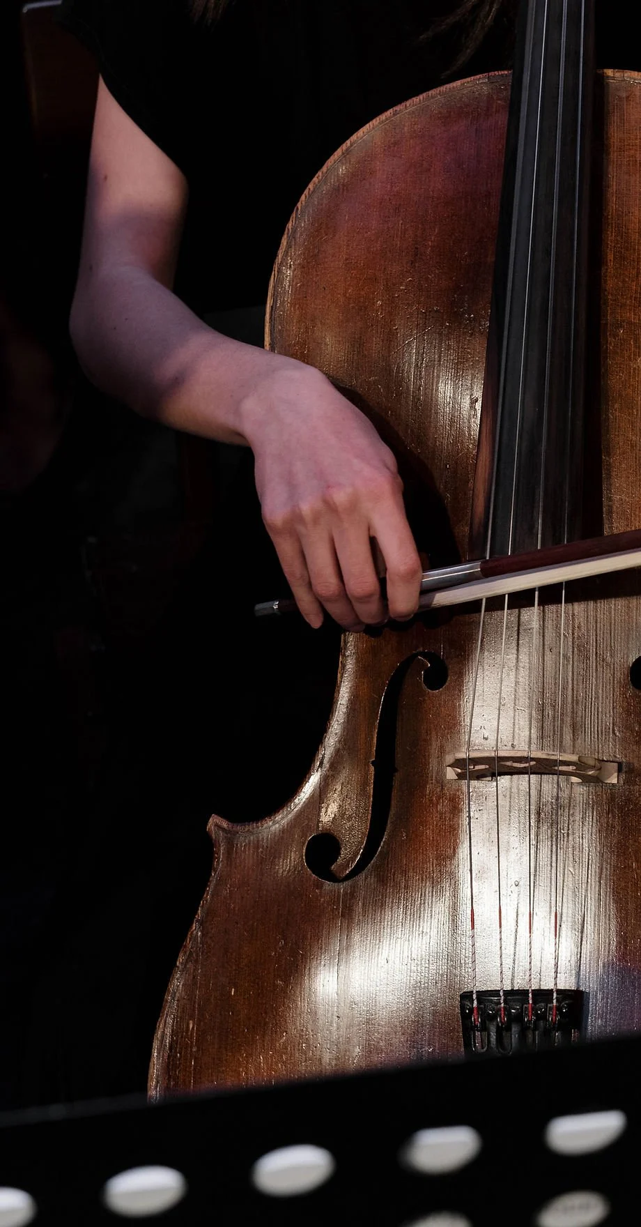 Mano che suona un violoncello in un ambiente basso di illuminazione.
