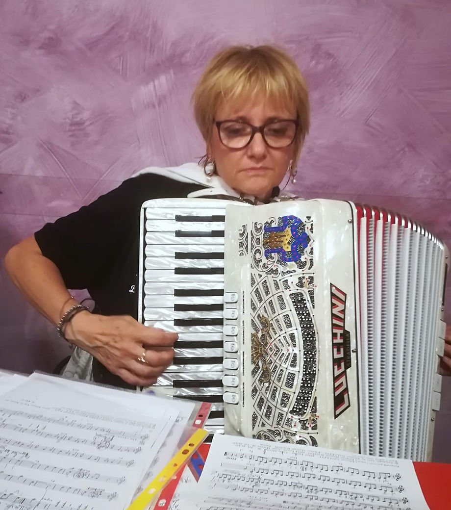 Una donna con capelli corti castani e occhiali guarda verso il basso mentre suona un armonica a bocca. Davanti a lei ci sono pagine di spartiti musicali.