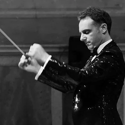 Maestro d'orchestra che conduce con bacchetta in un ambiente da concerto.