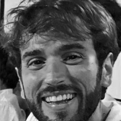 Primo piano di un uomo con barba, capelli corti e sorriso.