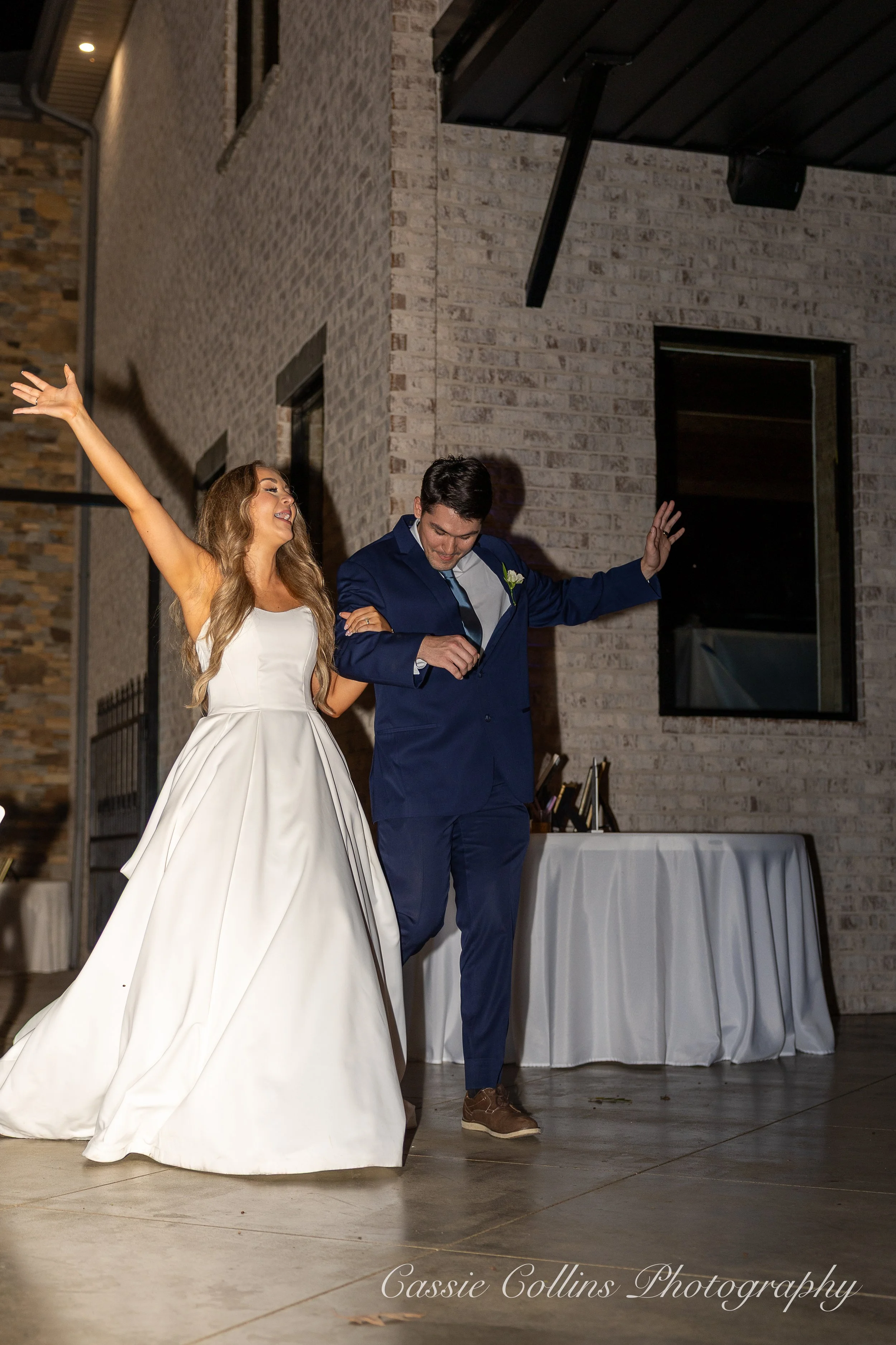 A bride and groom dancing at their wedding reception indoors, with the bride wearing a white wedding dress and the groom in a navy blue suit.