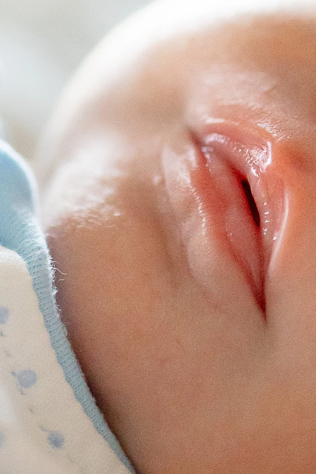 Close-up of a newborn baby with lips slightly open, lying on a blanket.