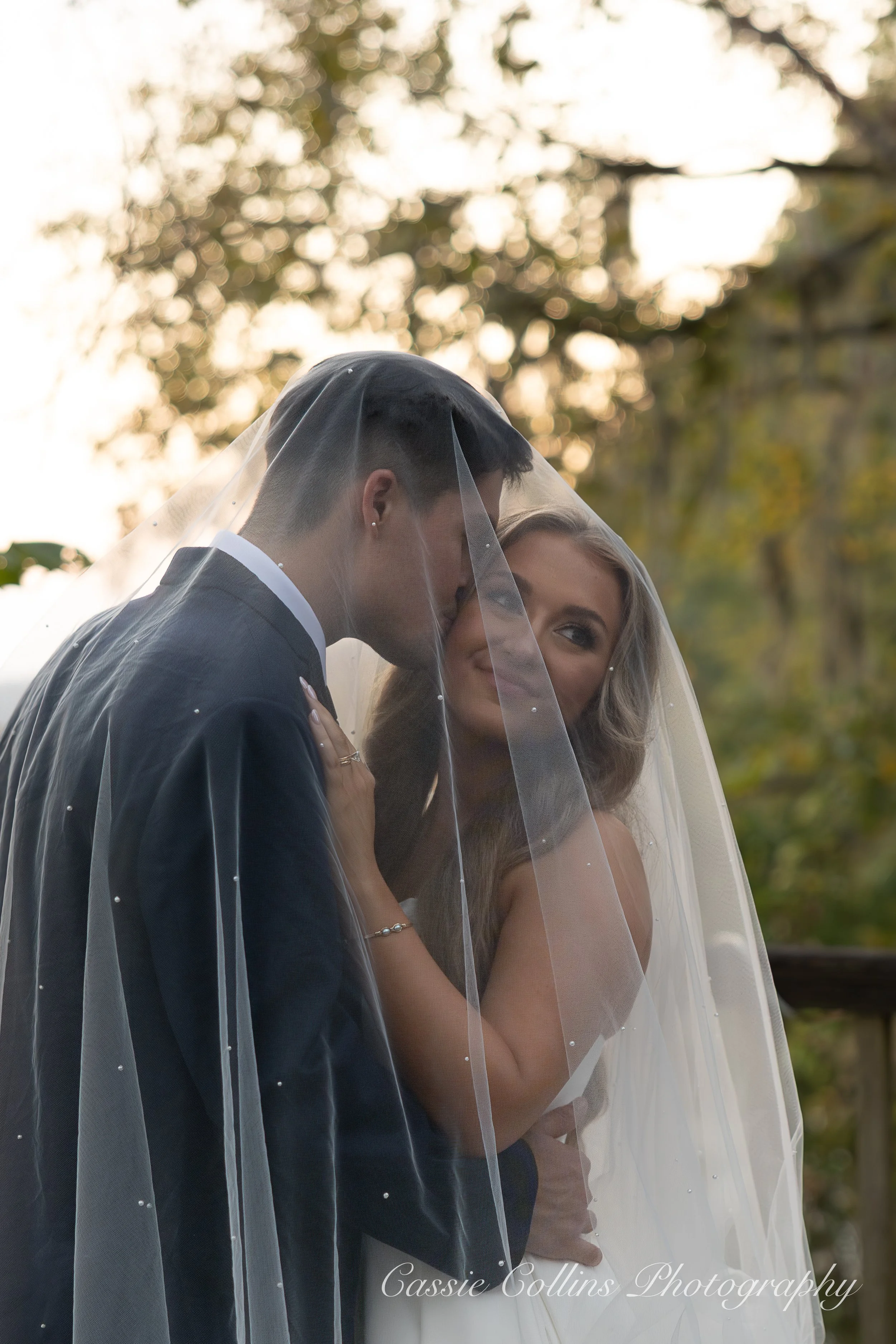 A bride and groom under a veil on their wedding day outdoors during sunset.